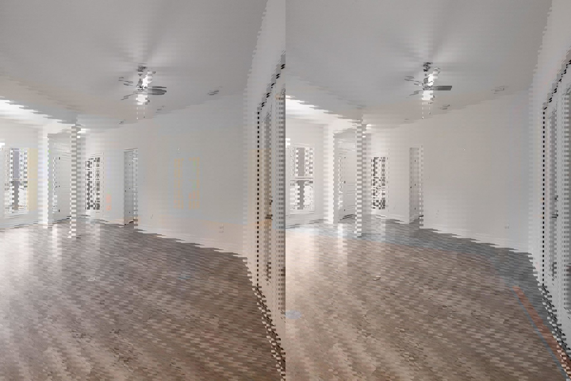 Spacious room featuring wood flooring, ceiling fan with light, white single and double doors with glass panes, window overlooking trees, and light switch on wall.