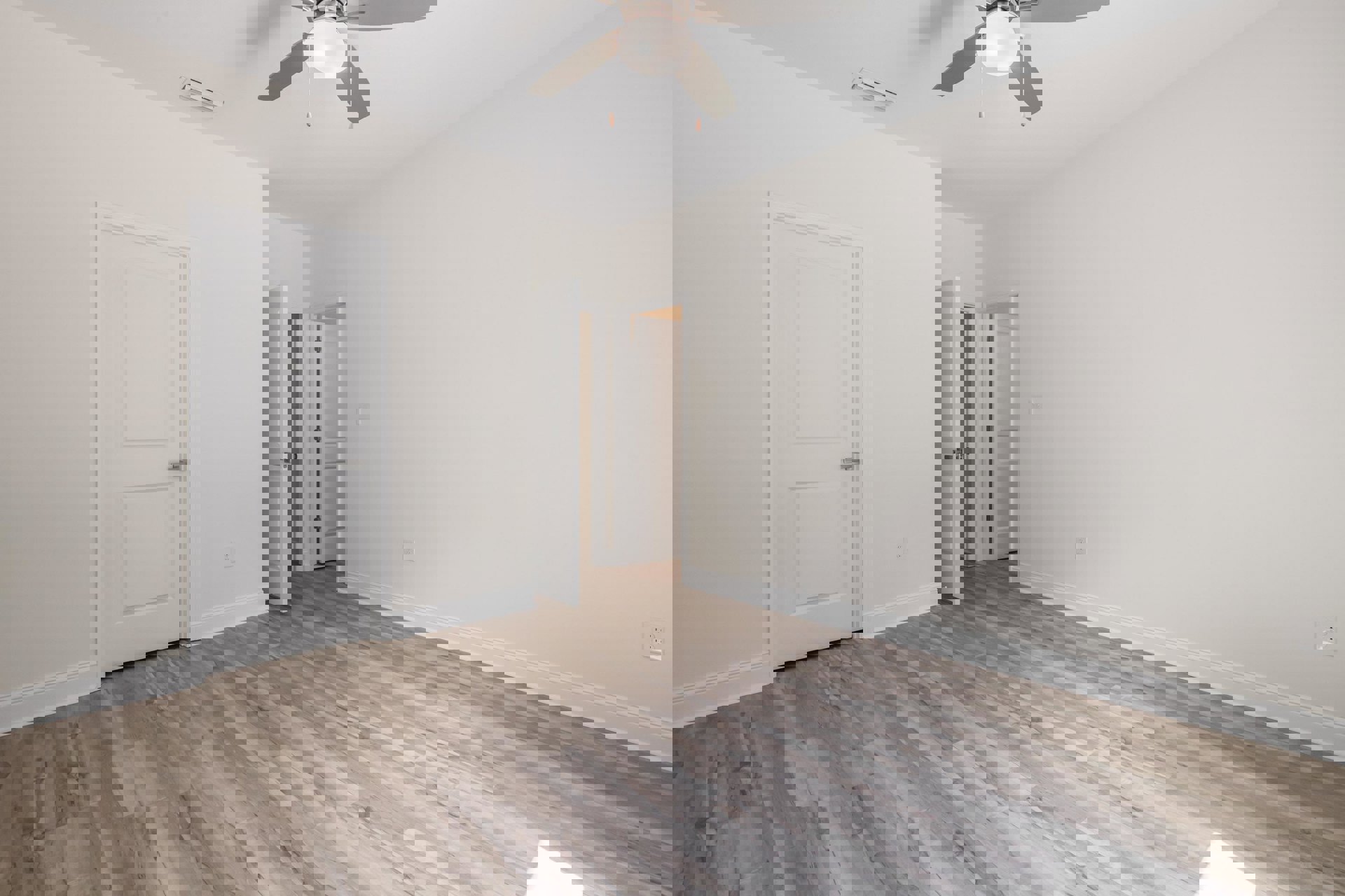 Ceiling fan with light fixture above wood flooring, white walls, and a white door with silver handle and metal hinge