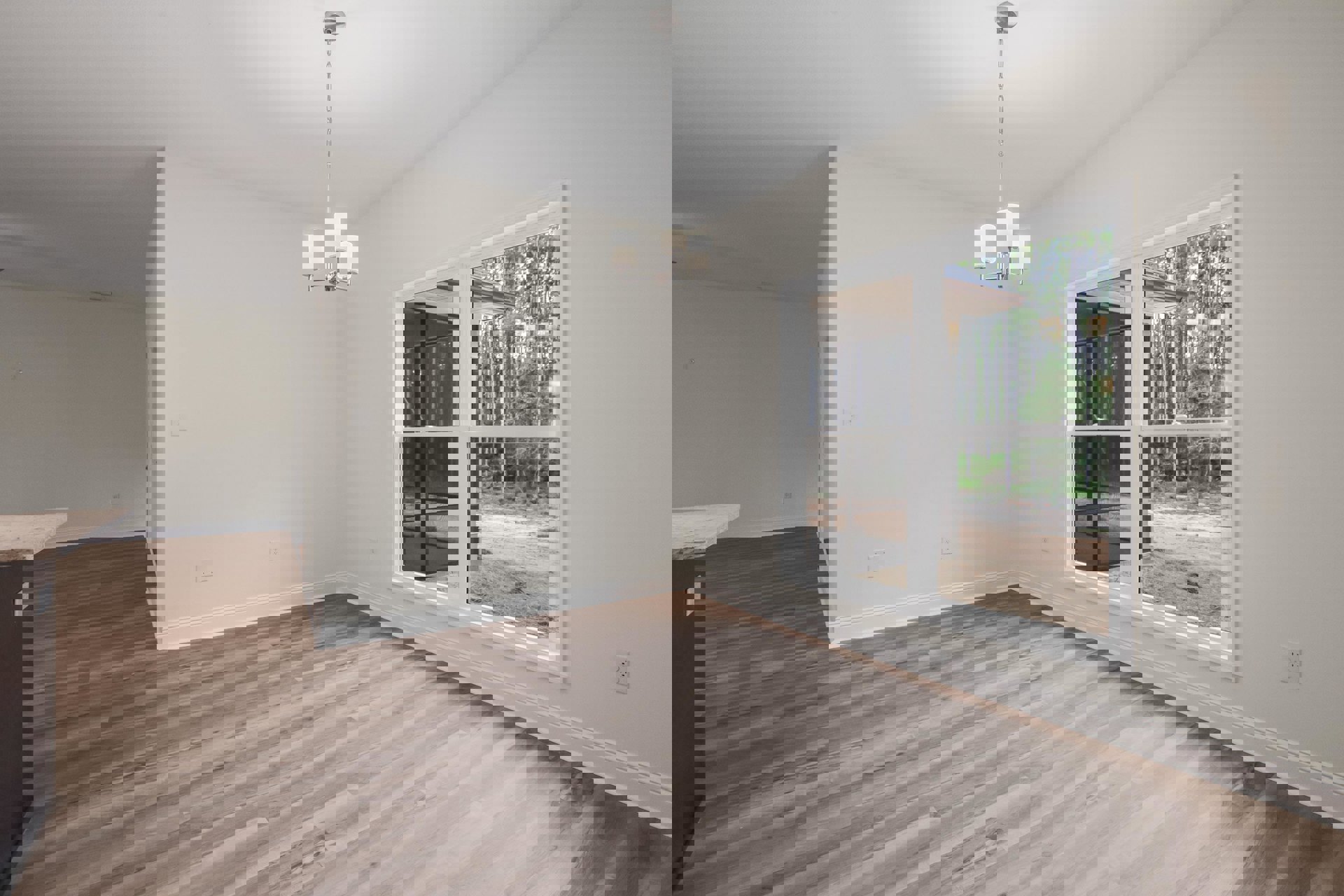 Wood flooring in a bright room with a large window overlooking a forest, white plaster walls, and a ceiling light fixture suspended by a long silver chain