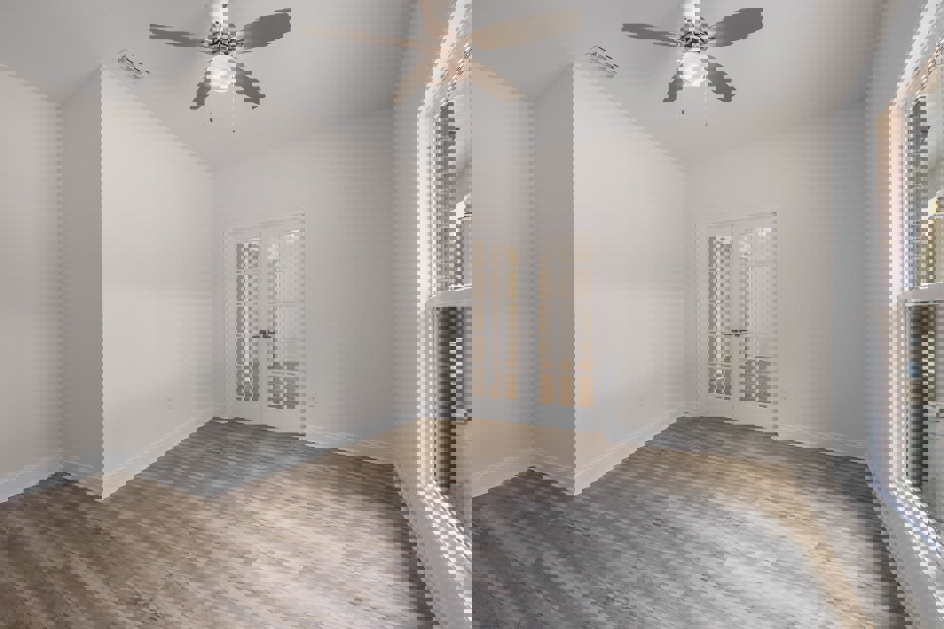 Ceiling fan with light fixture above wood flooring, white walls, and glass-paneled French doors leading outside
