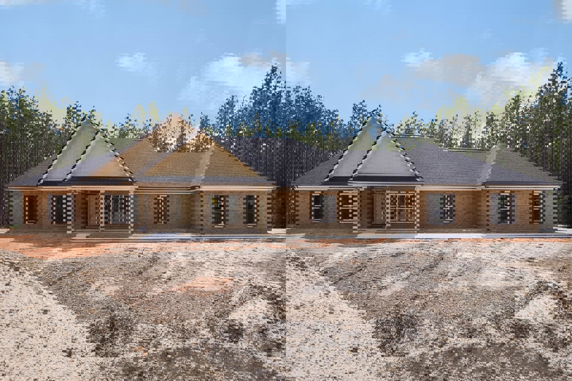 Partially built brick house with white roof, white-framed window, and white door, surrounded by dirt ground and trees in the background
