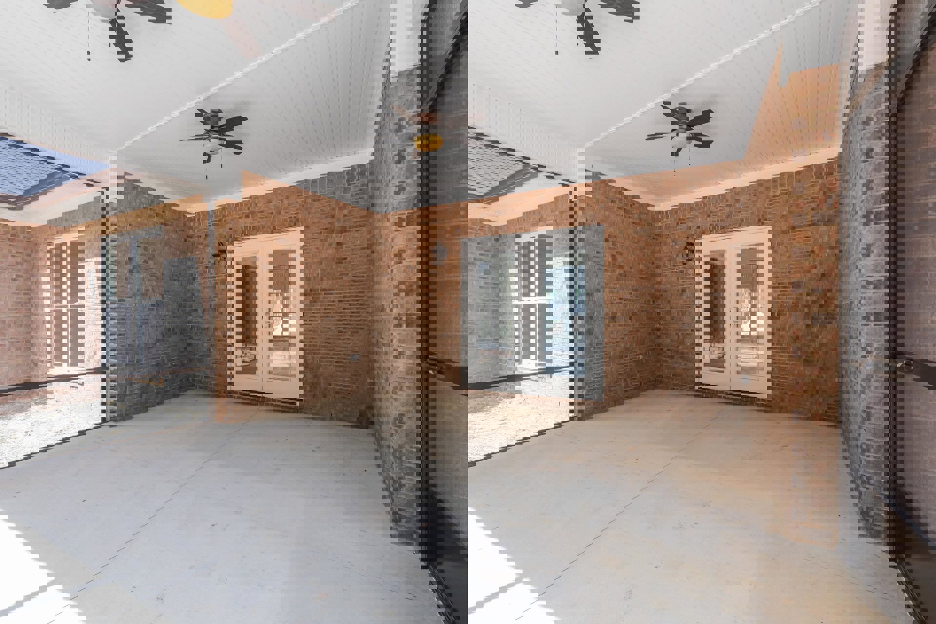 Living room with exposed brick accent wall, glass double doors, ceiling fan with illuminated light fixture, and hardwood flooring.