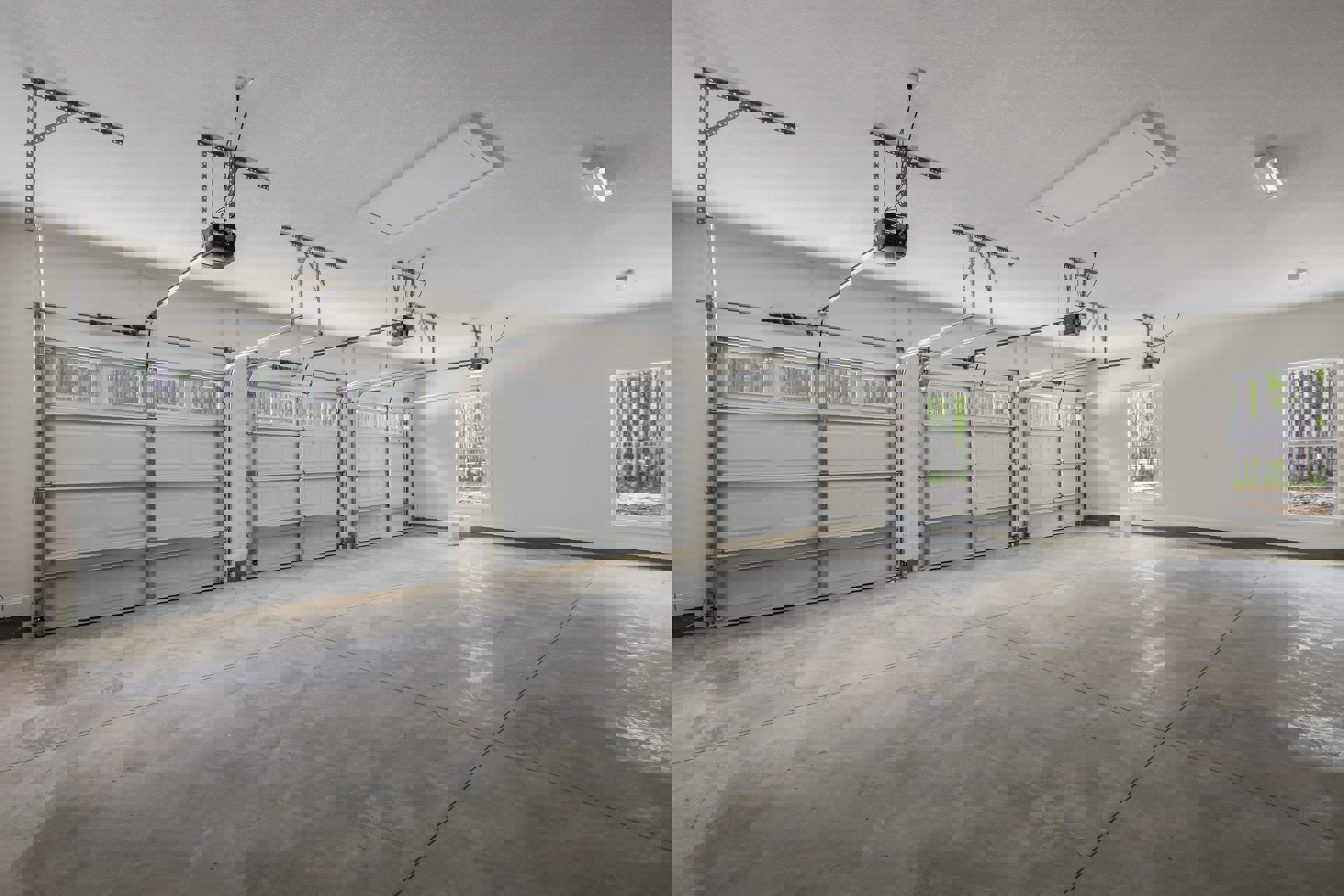 Spacious garage interior featuring multiple white garage doors with upper windows, smooth concrete floor, white walls, ceiling-mounted mechanical fan, and a window overlooking