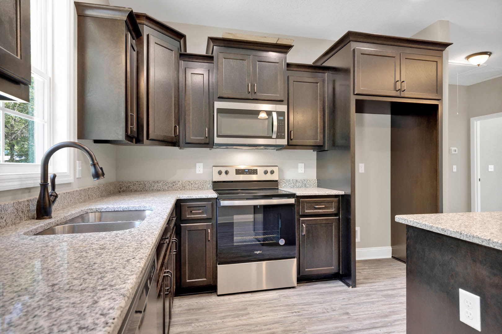 Dark wood kitchen cabinets with polished granite countertops, stainless steel oven and microwave, illuminated microwave display, chrome faucet and deep sink, close-up of oven