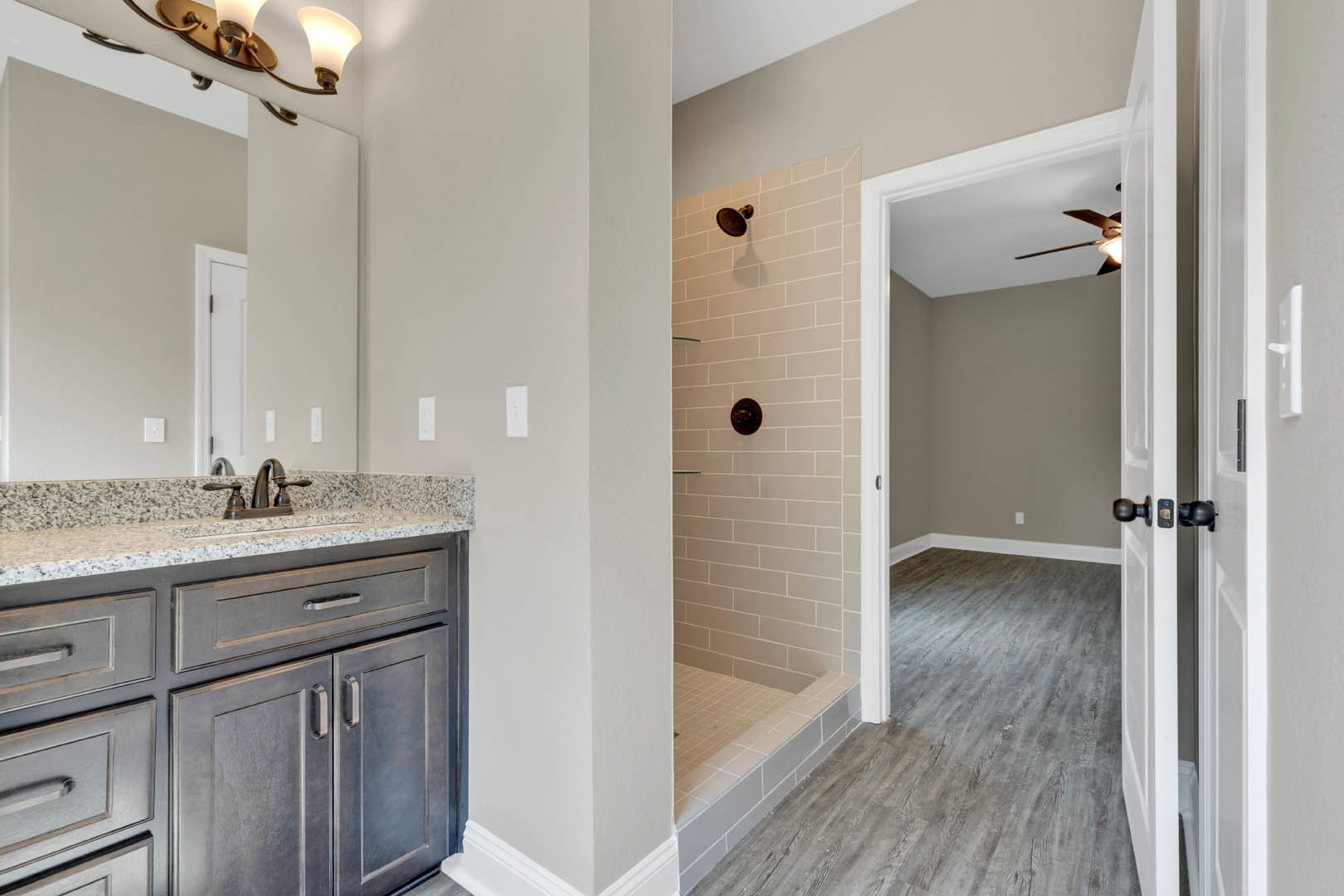 Bathroom featuring a tile shower wall with chrome shower head, granite countertop sink, and white cabinetry