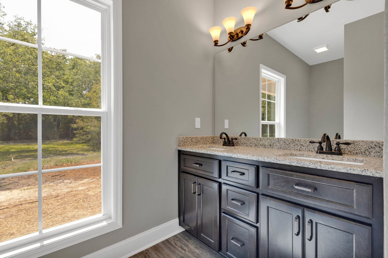 Bathroom with double sinks, expansive mirror, black cabinetry, stone countertop, and window overlooking field and trees