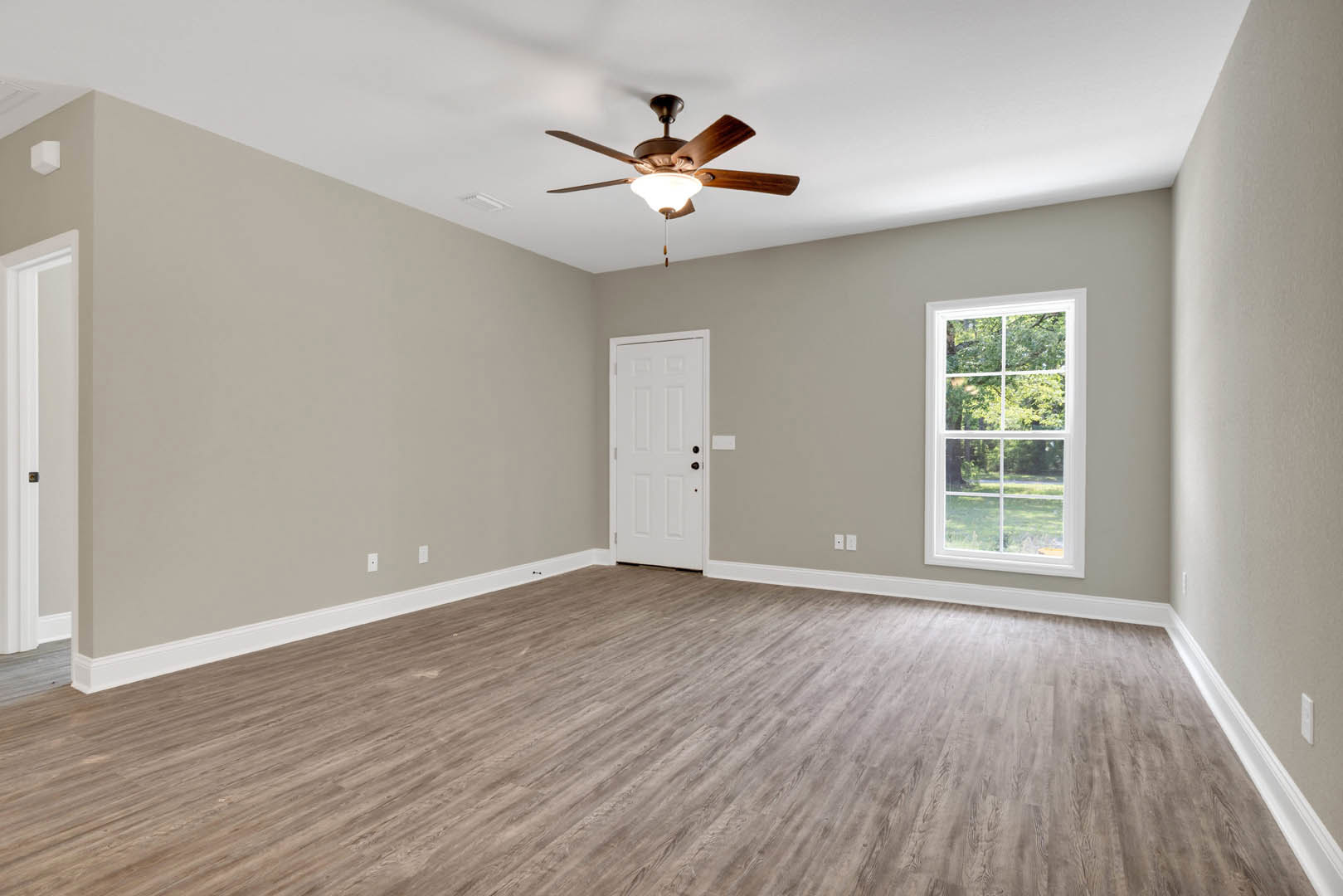 Bedroom with wood flooring, white walls, ceiling fan with light fixture, large window overlooking trees, and white door with black hardware