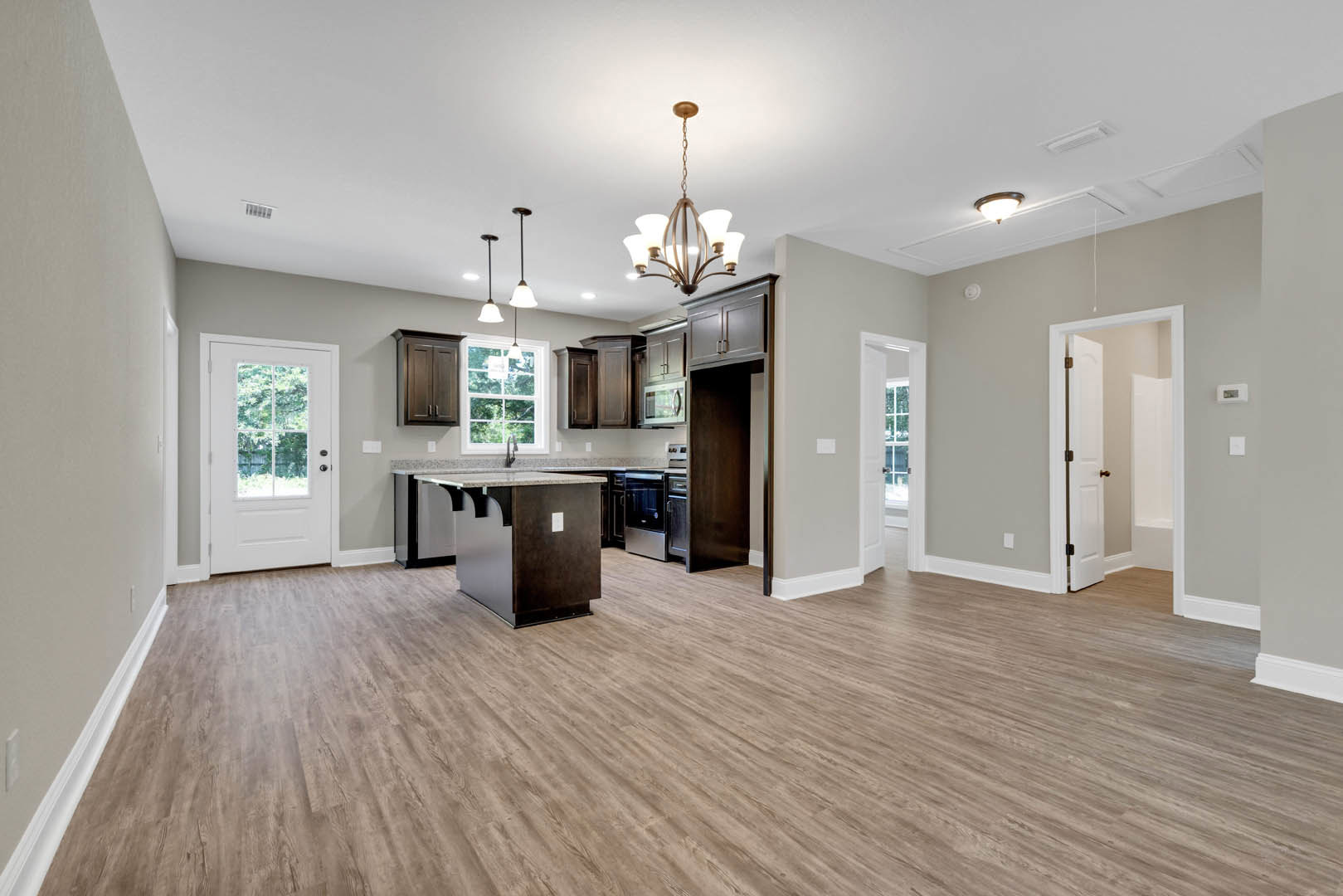 Open kitchen and living room with hardwood floors, white walls, marble kitchen island, brass door knob on white door, and chandelier overhead.