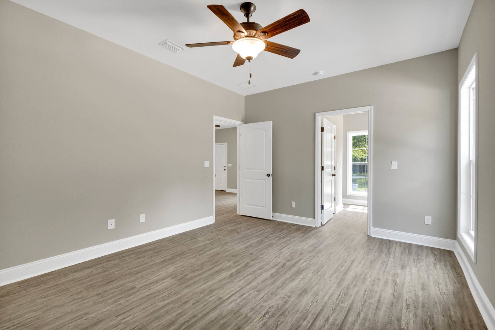Ceiling fan with integrated light fixture, wood laminate flooring, white paneled door with black handle, smooth plaster walls, natural light filtering through doorway