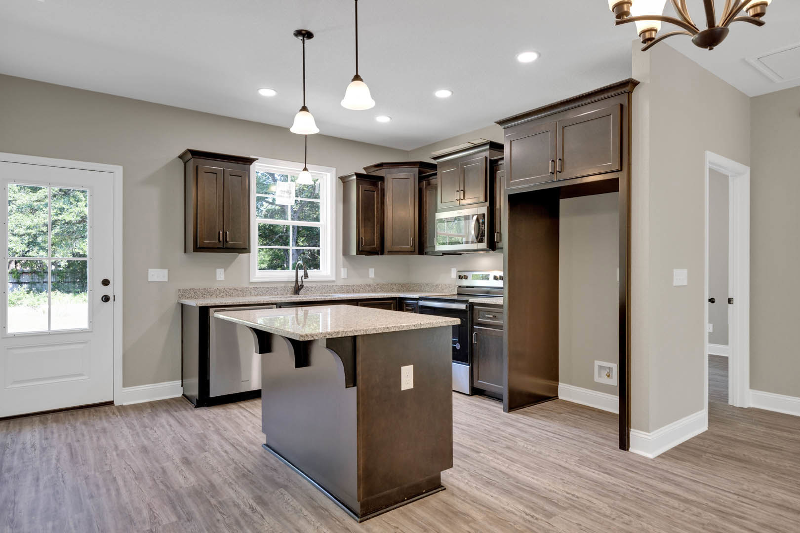 Open kitchen featuring a central island with granite countertops, white cabinetry, light fixture above the island, wood flooring, and a window with a white frame.