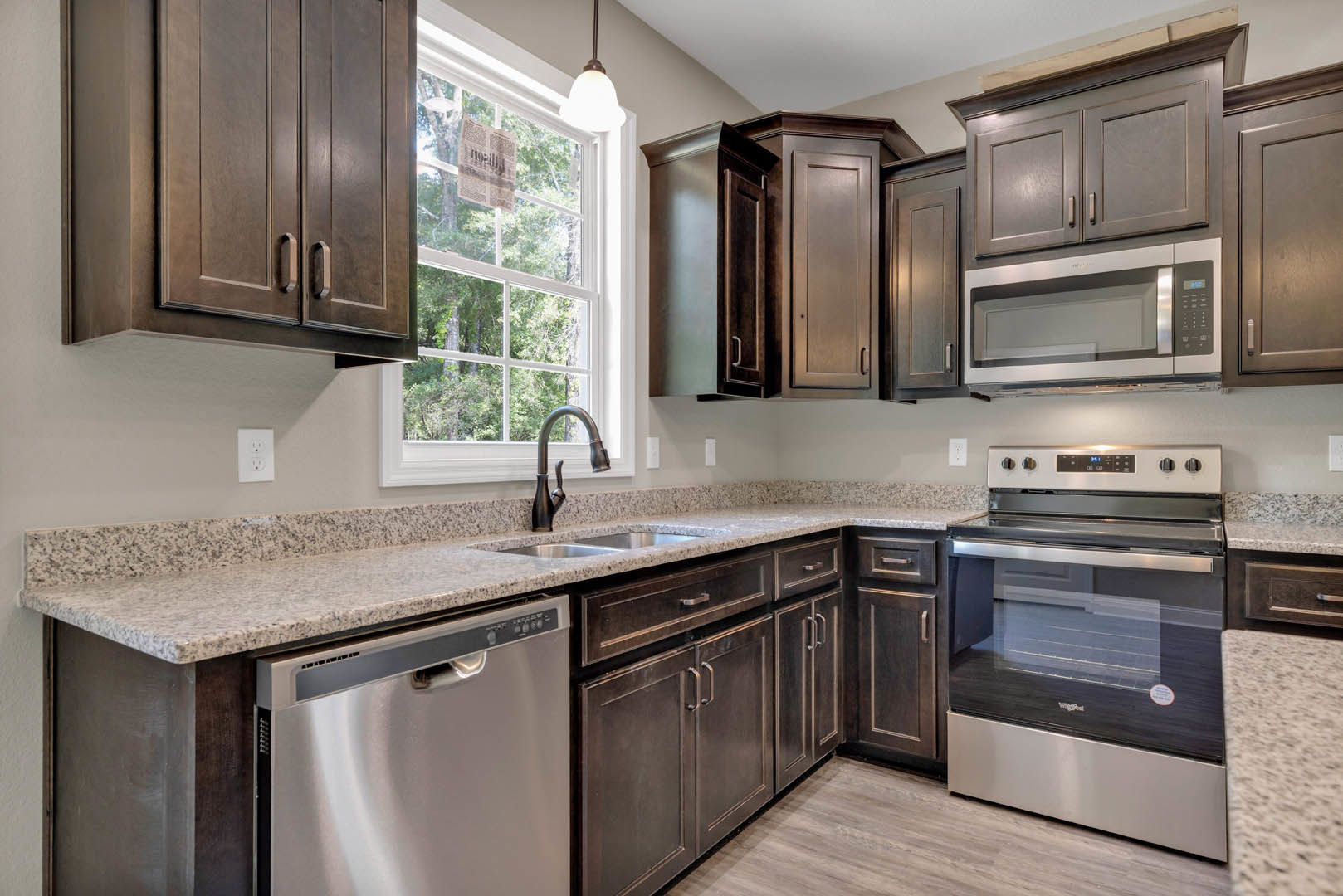 Dark wood kitchen cabinets, granite countertops, stainless steel oven and dishwasher, built-in microwave, white outlet with black buttons, newspaper wedged in window frame