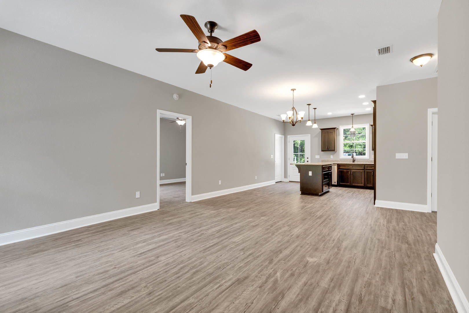 Open-concept room featuring wood flooring, a ceiling fan with light, white walls, and a kitchen island with light countertops