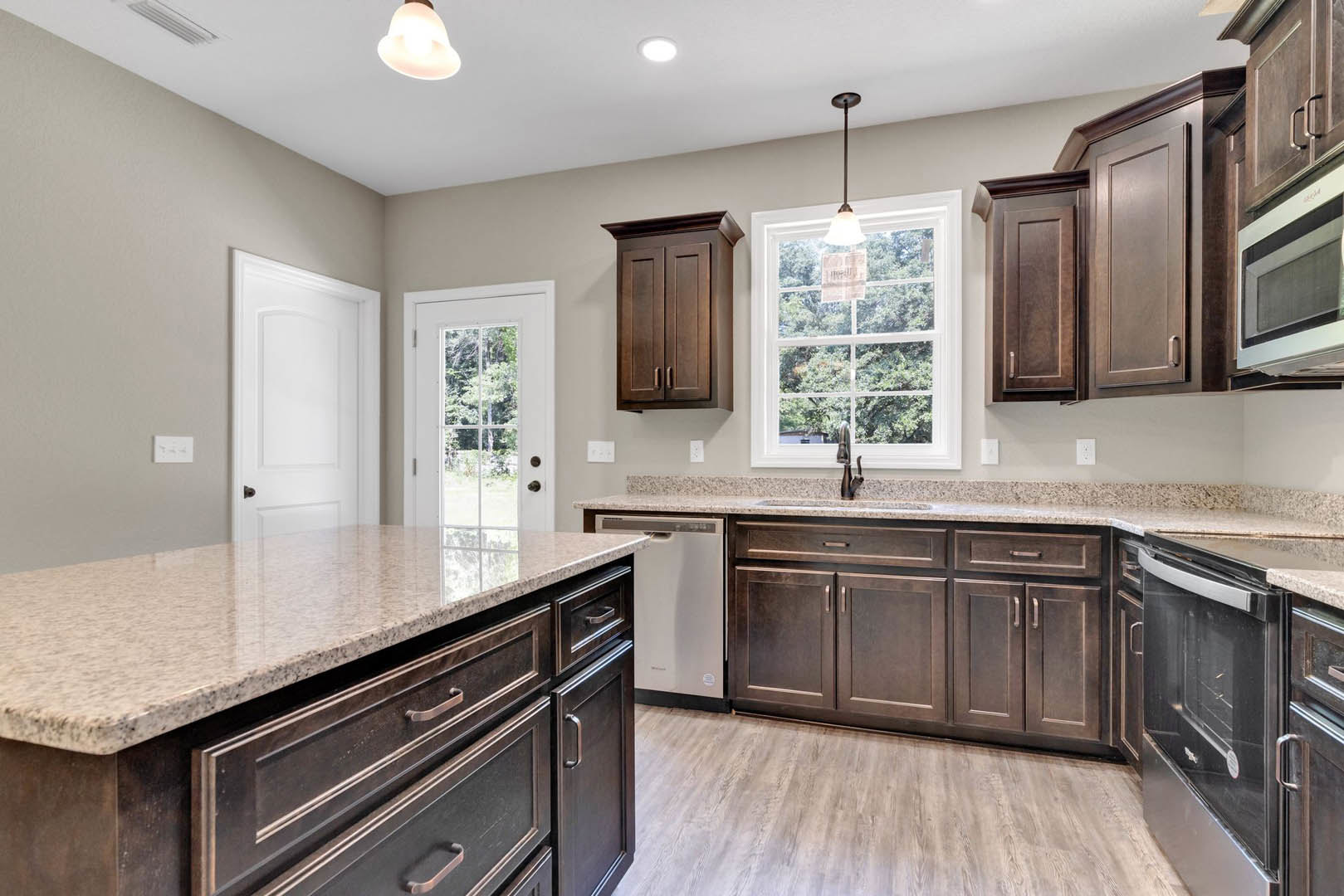 Kitchen with dark wood cabinets, granite countertops, stainless steel sink, white door with matching frame, window featuring a sign, and modern pendant light fixture