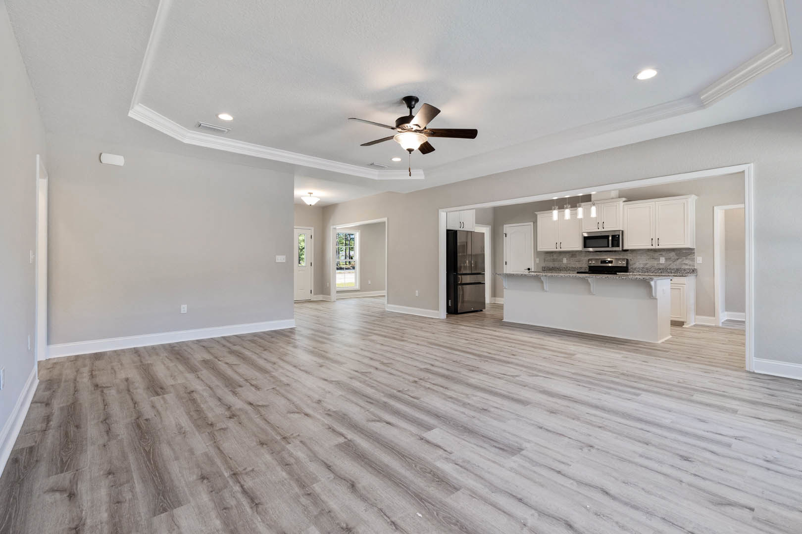 Spacious open floor plan featuring hardwood flooring, white walls with shelving, modern kitchen with stainless refrigerator, dining area, ceiling fan with light fixture, and large