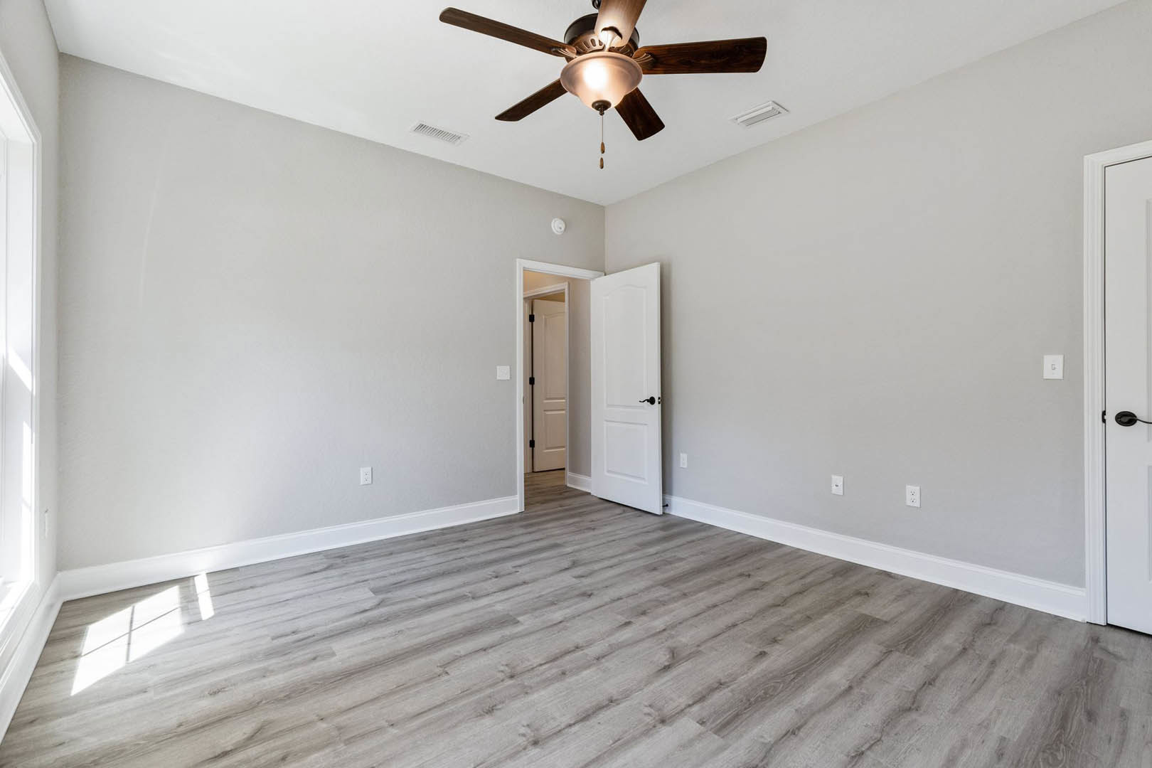 Ceiling fan with light fixture mounted above wood flooring, white door with black handle, neutral walls, and simple molding.