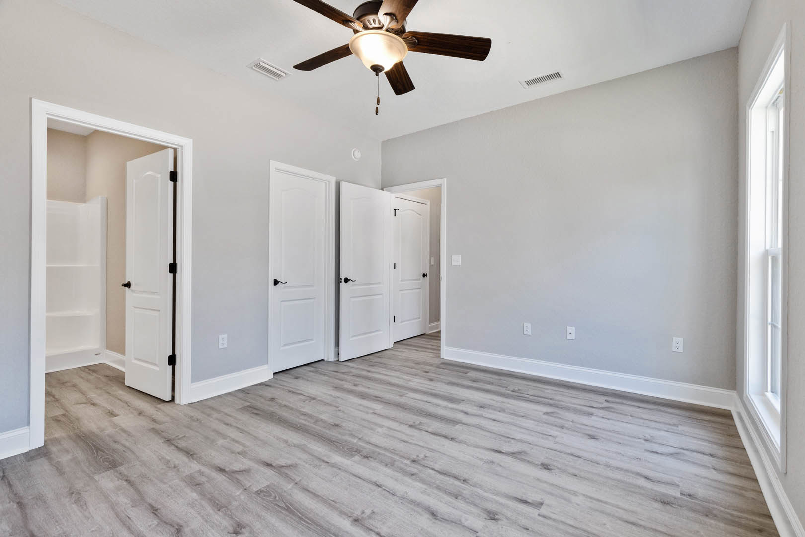 Room with wood flooring, white paneled doors featuring black handles, plaster walls, and a ceiling fan with integrated light fixture.