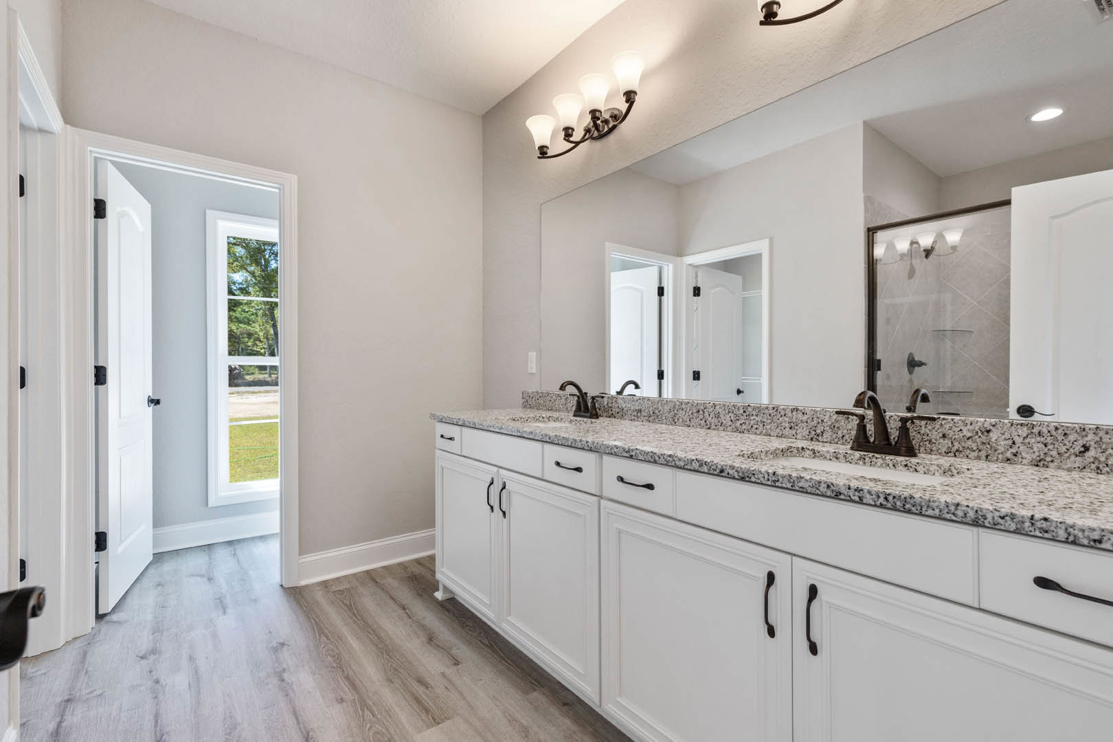 Bathroom featuring white cabinetry, marble countertops, glass shower door, modern light fixture, and a door opening to a yard; white walls with black trim and tiled flooring.