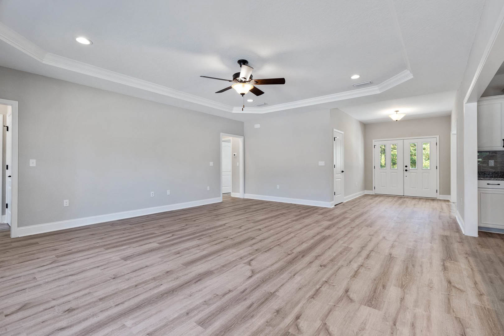 Ceiling fan with light fixture above hardwood floor, white double doors with glass panes, neutral walls, and baseboard trim