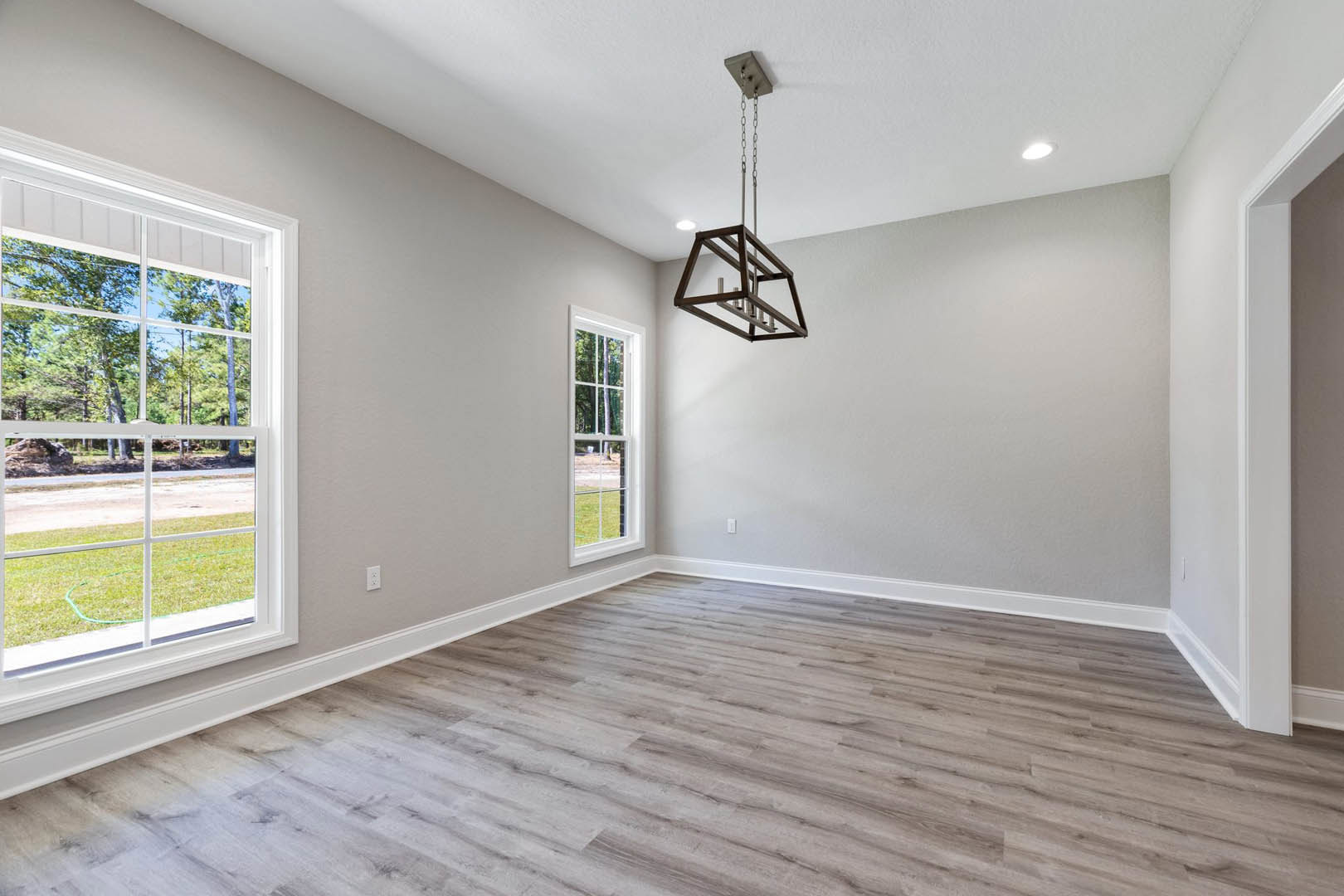 Wood flooring in a spacious room with large windows overlooking trees, metal ladder descending from ceiling, and chandelier hanging above.