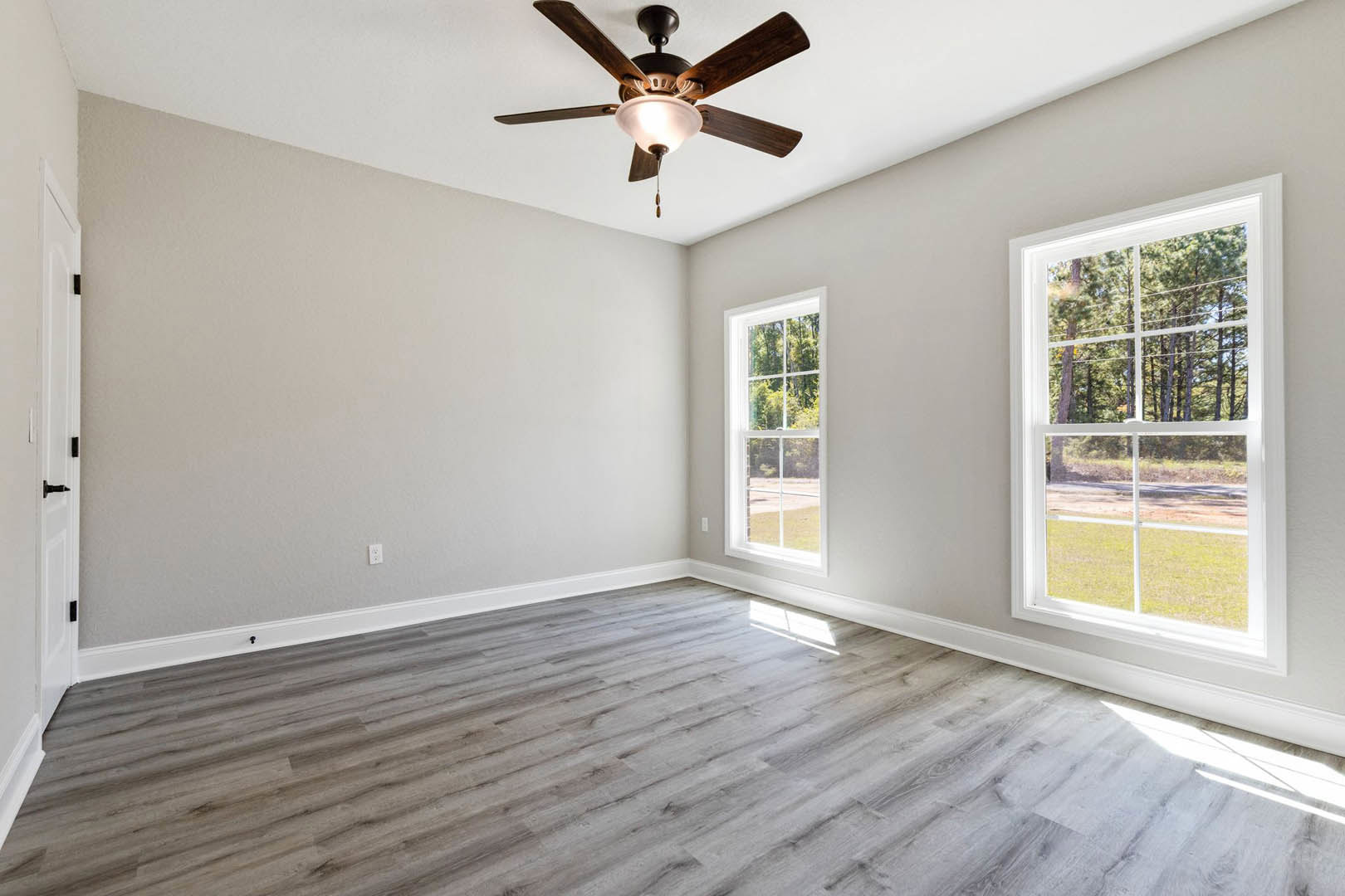 Ceiling fan with integrated light fixture, wood flooring, plaster walls, large windows framing leafy trees outside