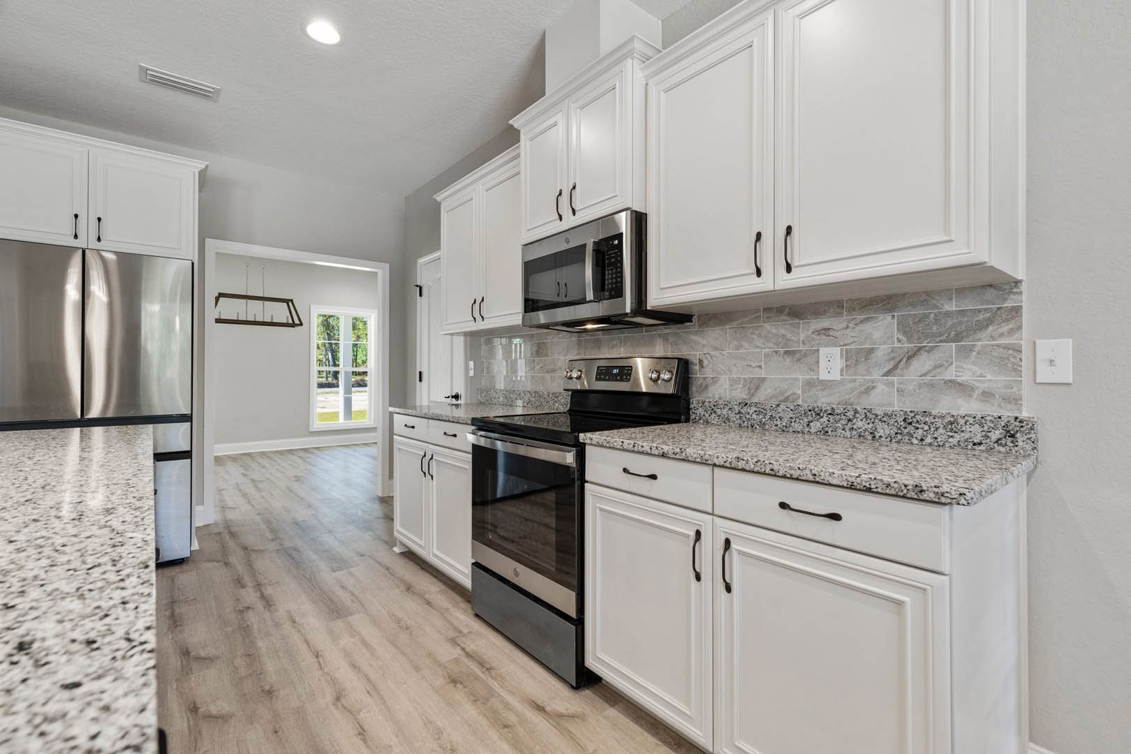 White kitchen cabinets with granite countertops, black oven, built-in microwave, stainless steel refrigerator, ceiling light fixture, and wall-mounted light switch