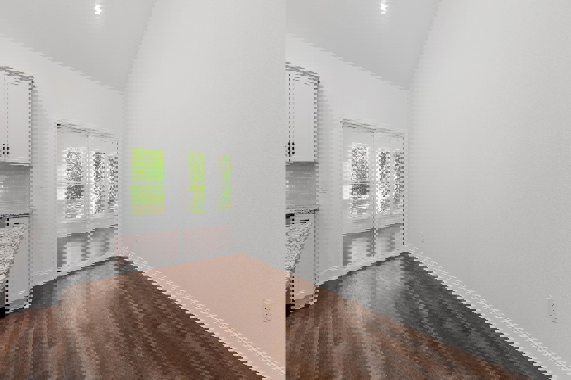 Sliding glass door framed by white trim, wood flooring, white cabinetry with black handles, and a stone countertop; trees visible through the door.