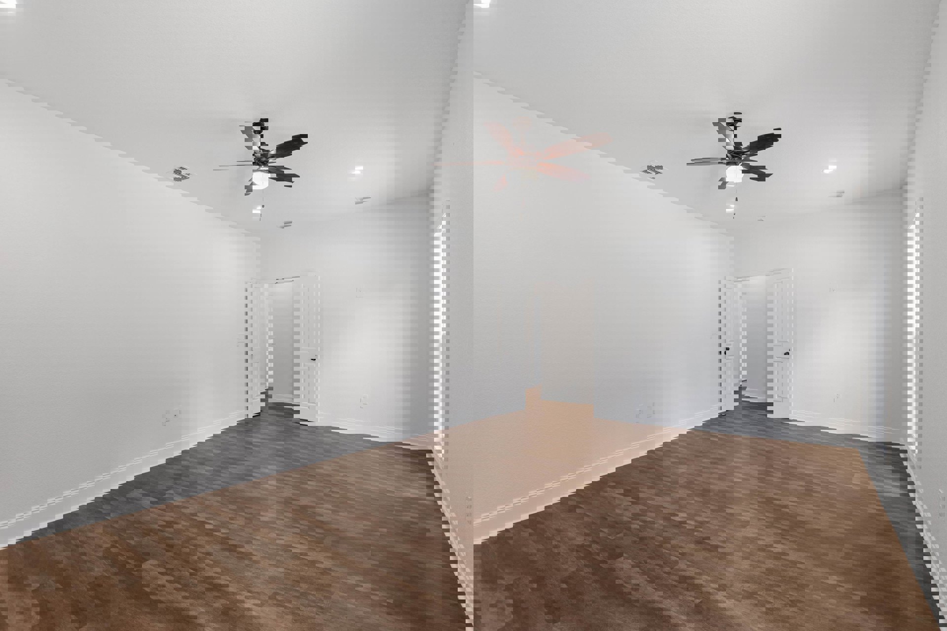 Ceiling fan with light fixture, wood laminate flooring, white door with black knob, smooth plaster walls