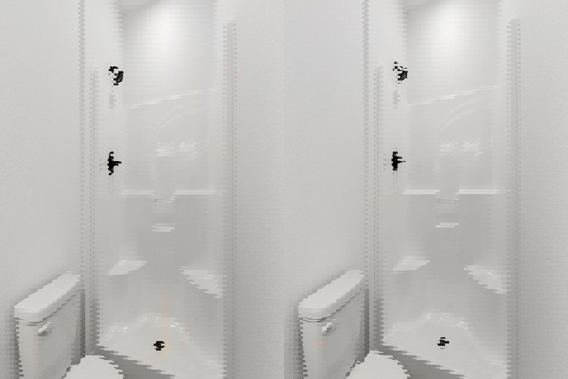 White tiled shower with curved chrome shower head, built-in drain, and adjacent white toilet in a bright bathroom.