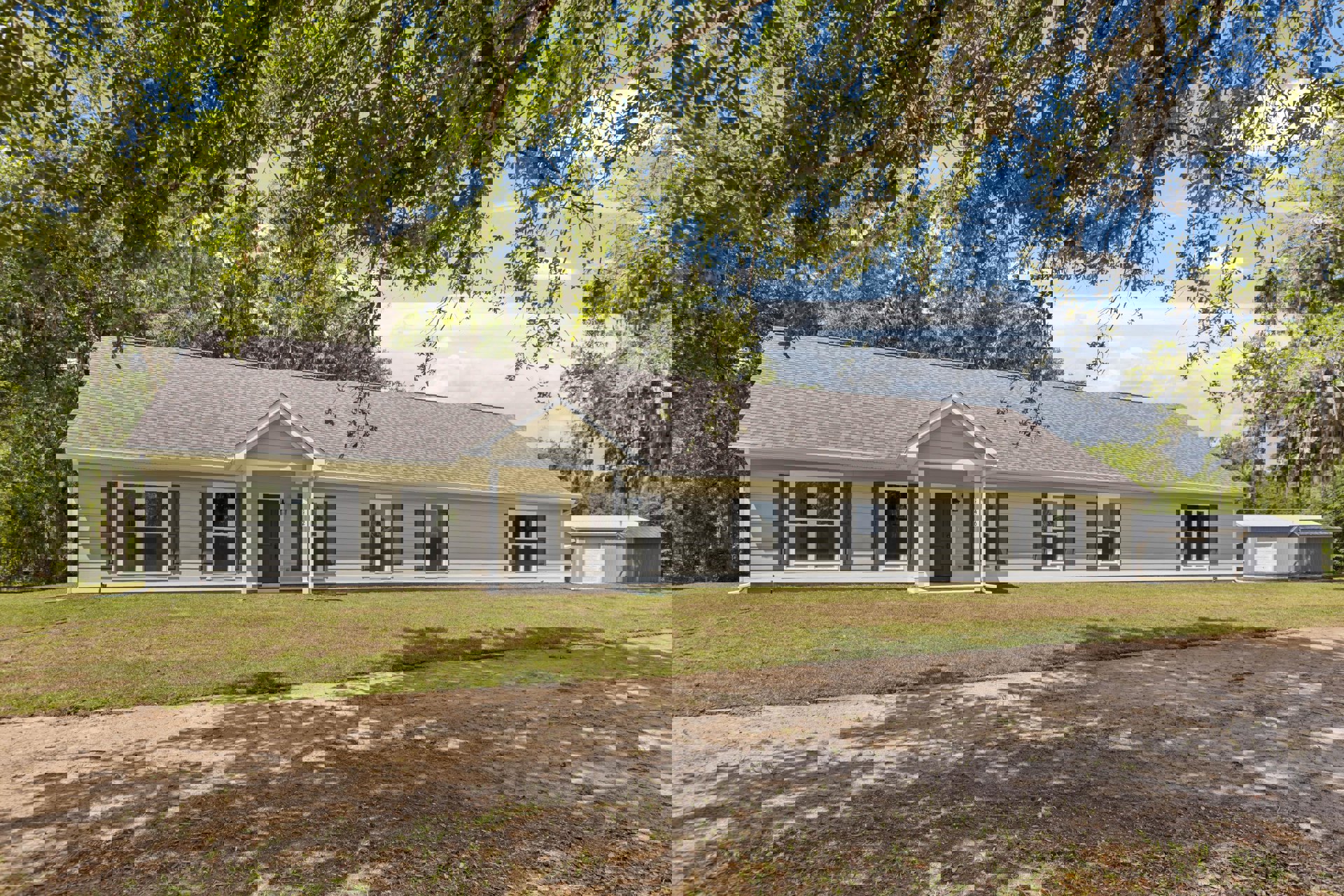 Two-story house with white-framed windows, black front door, covered porch supported by white columns, dirt path leading across green lawn, mature trees in background