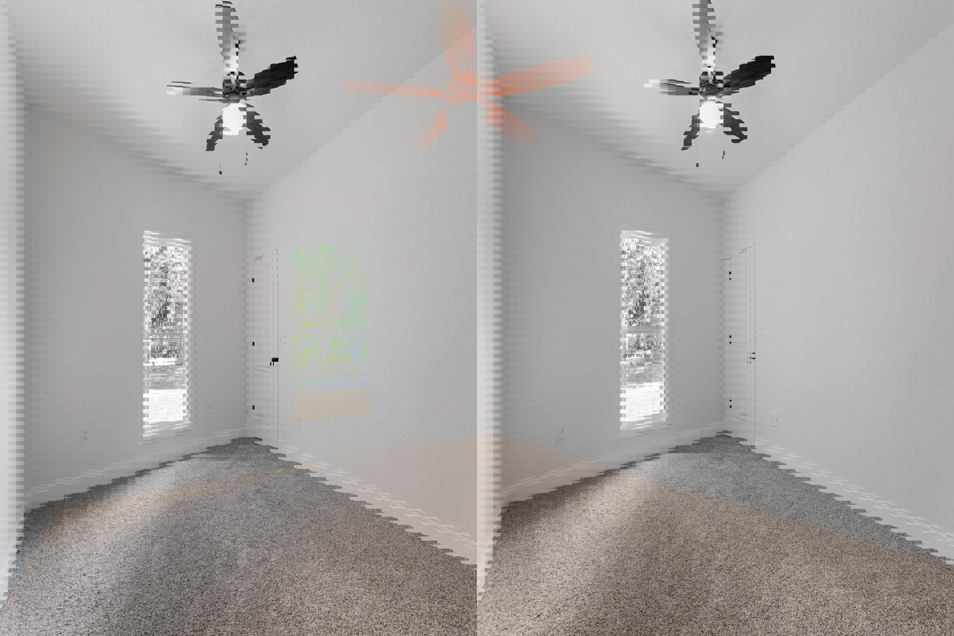 Bedroom with beige carpet, white walls, ceiling fan with light, white door with black knobs, large window showing green trees outside