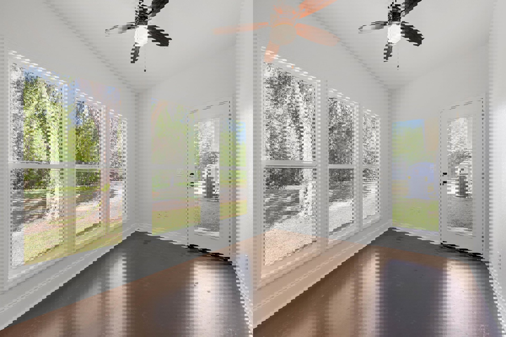 Ceiling fan with light fixture above brown laminate flooring, white walls, and glass doors opening to outdoor view of trees and grass