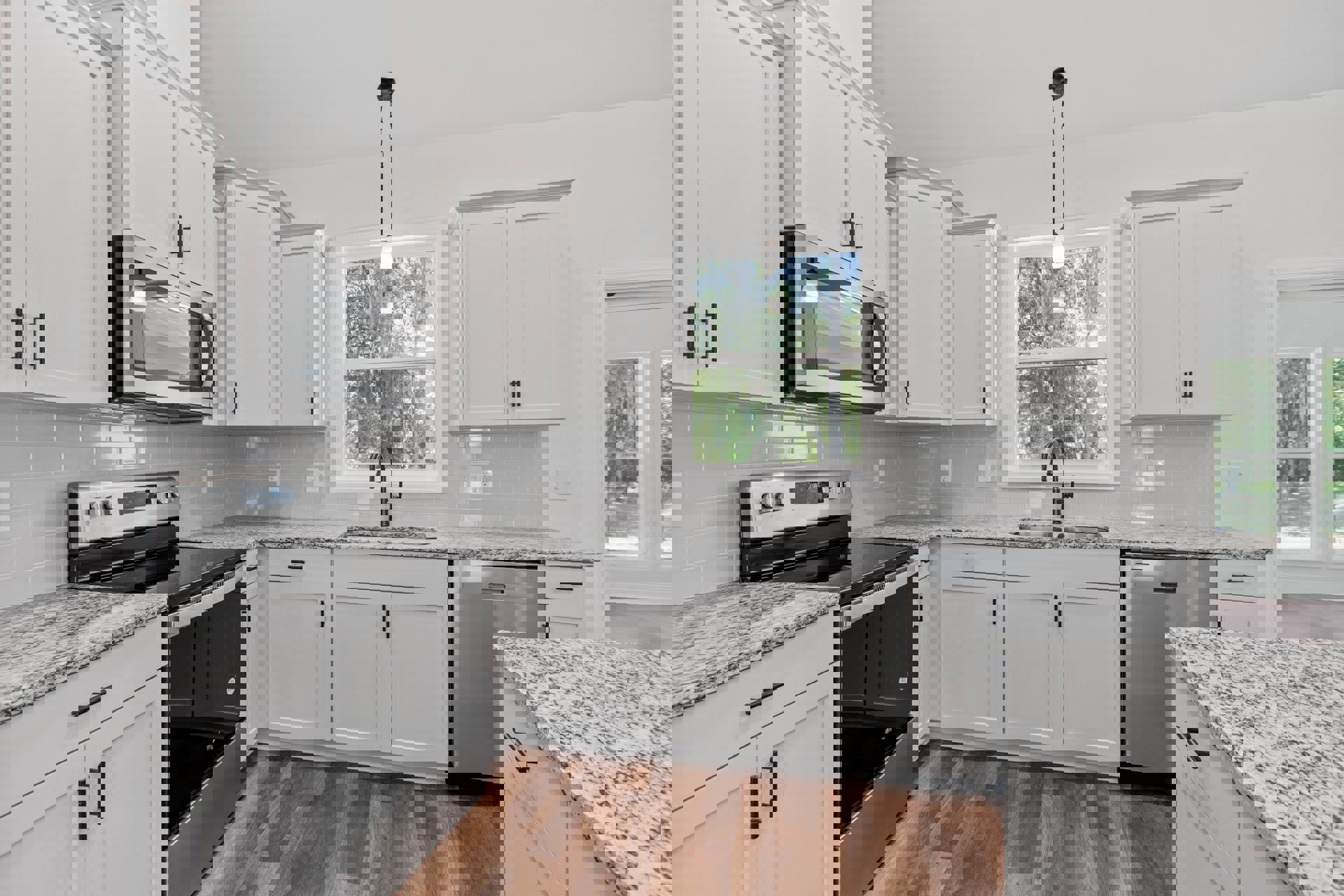 White kitchen cabinets with black appliances, including a stove, oven, and microwave; white countertop with black specks, black faucet, window showing trees outside.