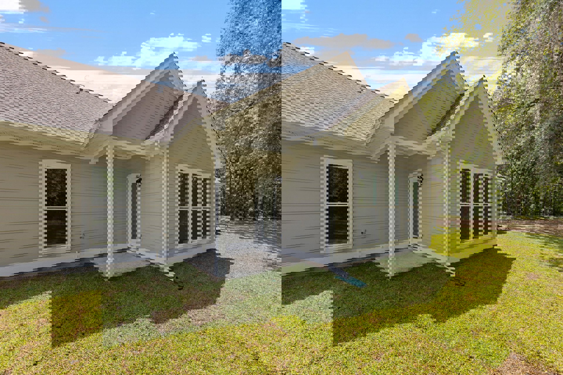 Two-story home with white siding, covered porch, white framed door, large windows, green lawn, and mature trees in the background