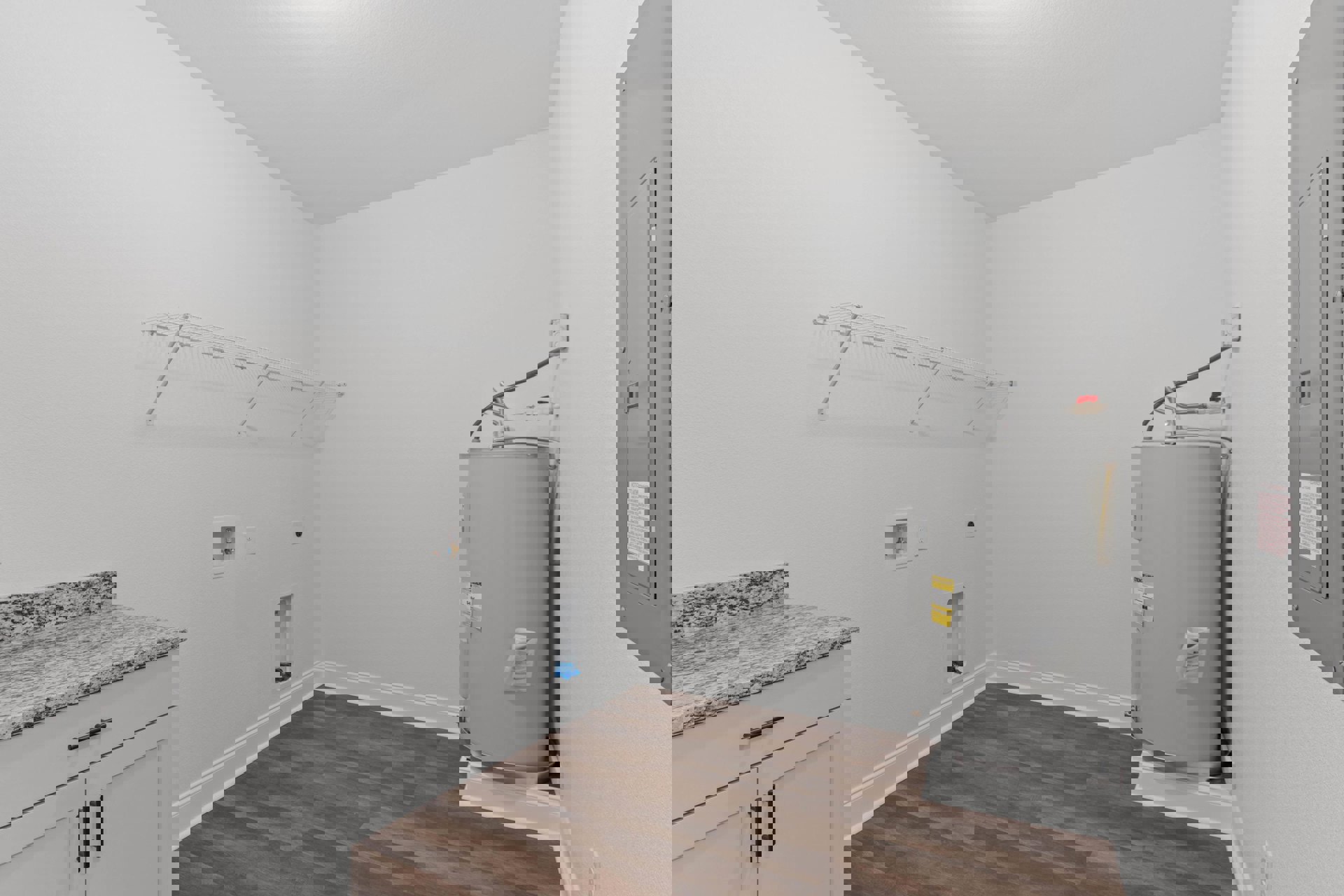 Laundry room with wood flooring, white baseboards, marble countertop, white shelving, large silver tank, and white cylindrical object with yellow label against white walls