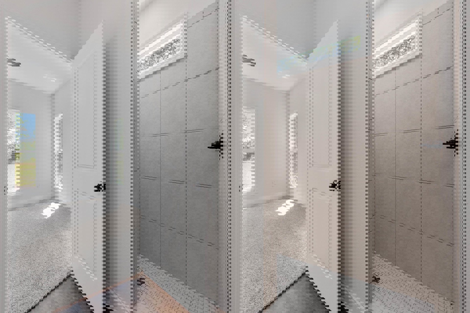 Bathroom with white carpeted floor, open white door featuring black knob, tiled shower with chrome shower head, window overlooking leafy tree, sunlight streaming onto carpet