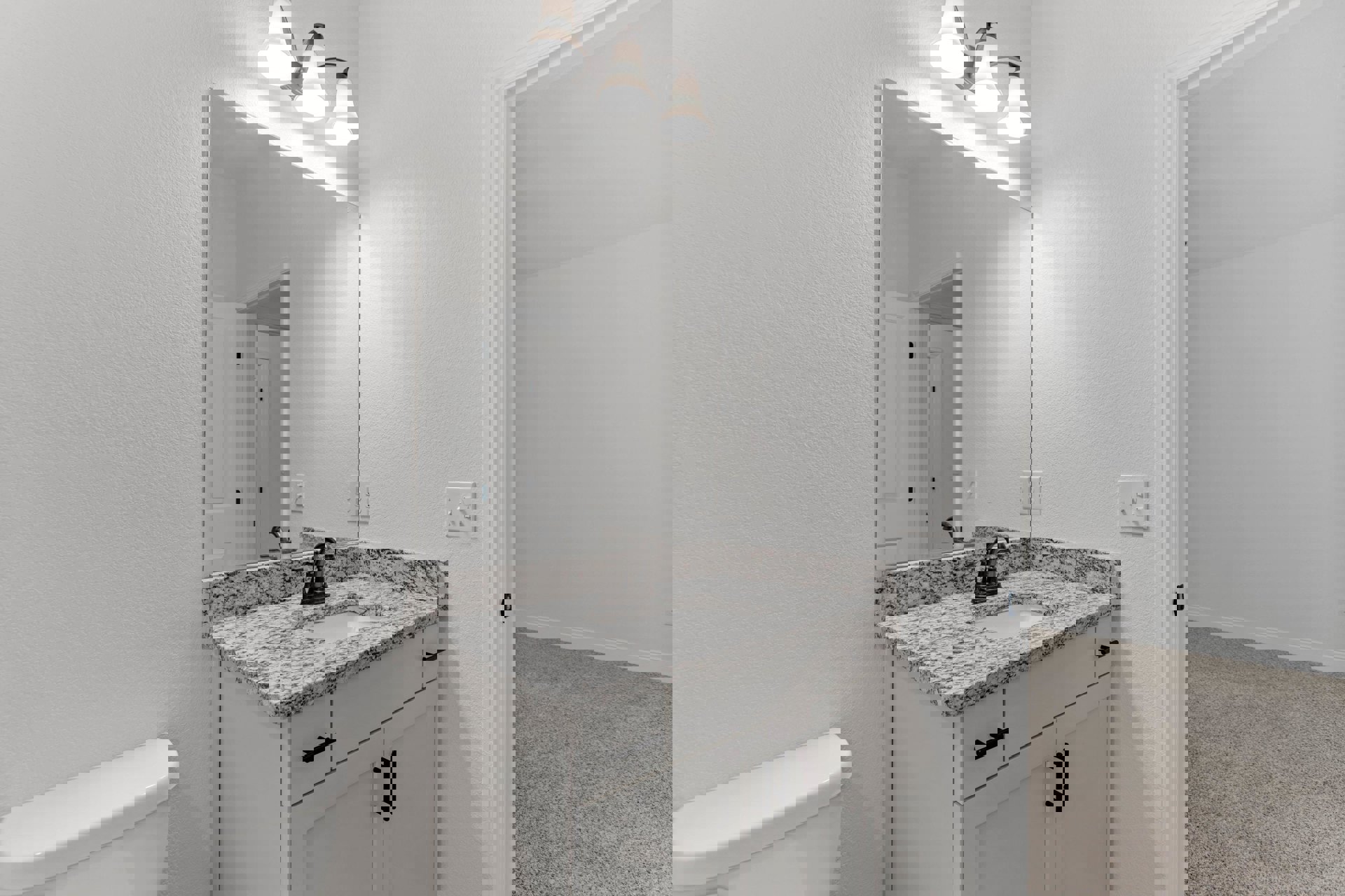 Bathroom with marble countertop, undermount sink, wall-mounted mirror, white toilet, chrome faucet, light fixture, black cabinet handle, and tiled walls