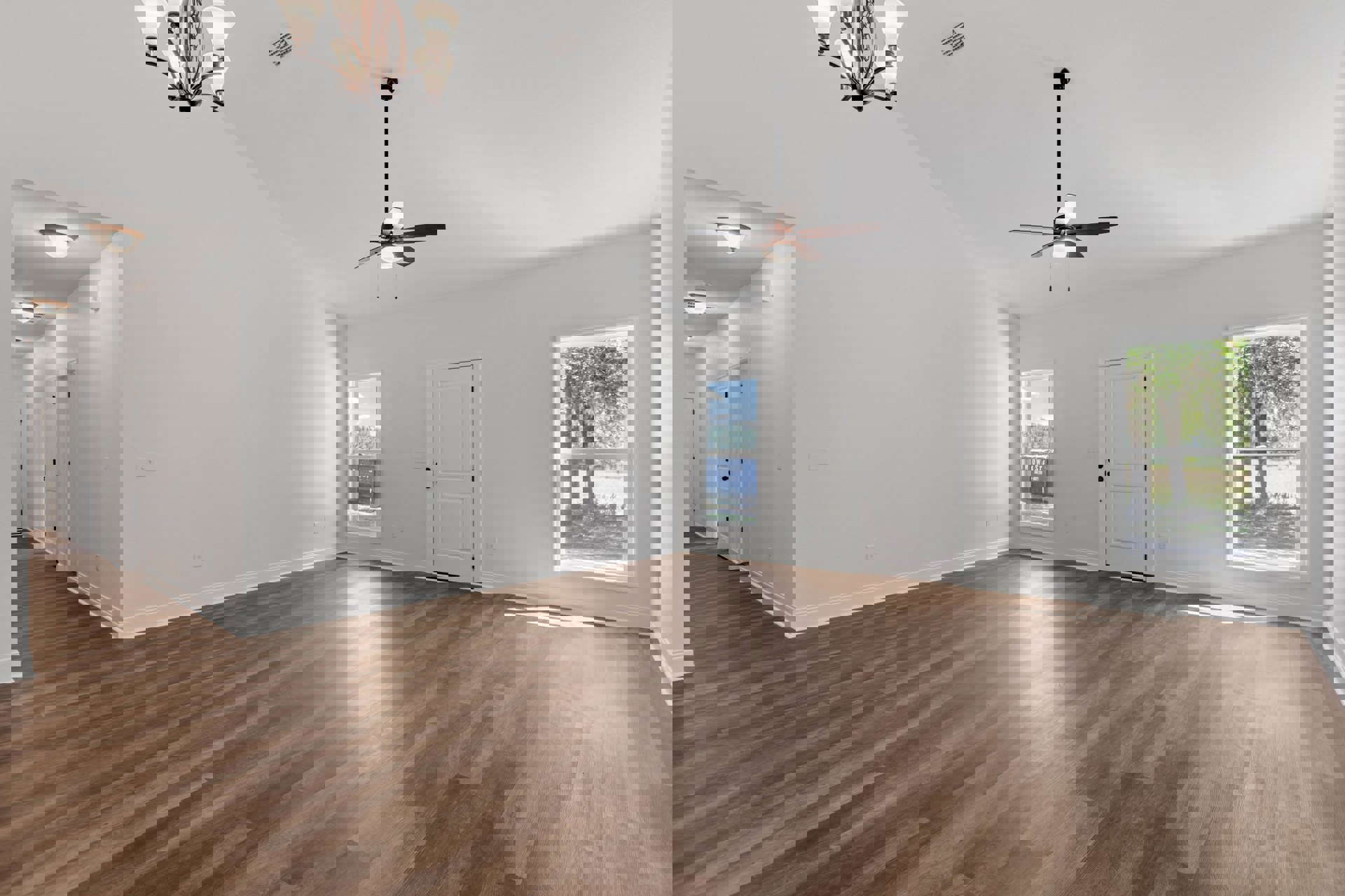 Ceiling fan mounted on white plaster ceiling above wood laminate flooring, white door with black knobs, large window revealing trees and outdoor container, close-up of modern