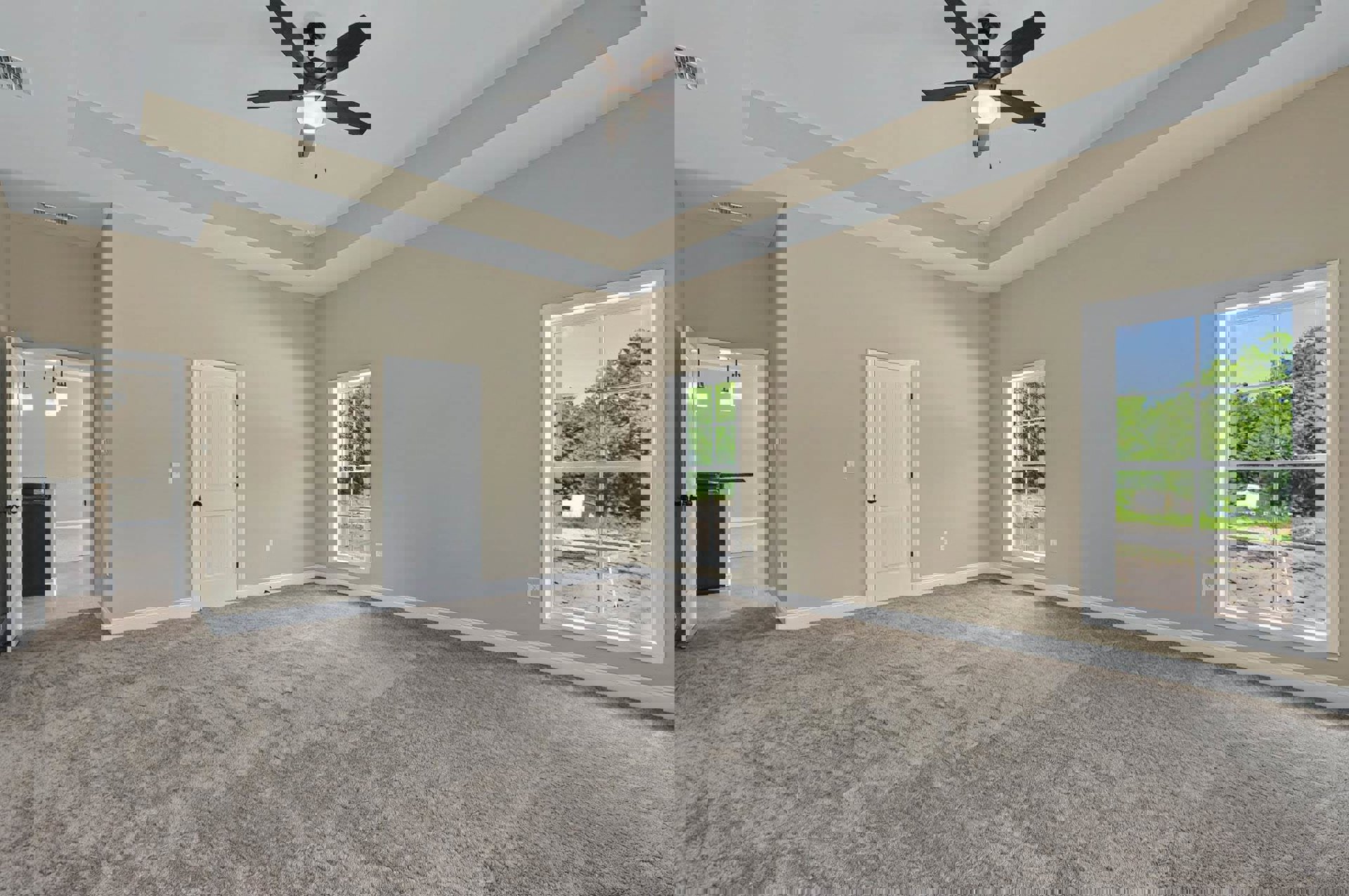 Carpeted room with a ceiling fan and light, white-framed window showing trees outside, white door with black knobs, pale walls and baseboards