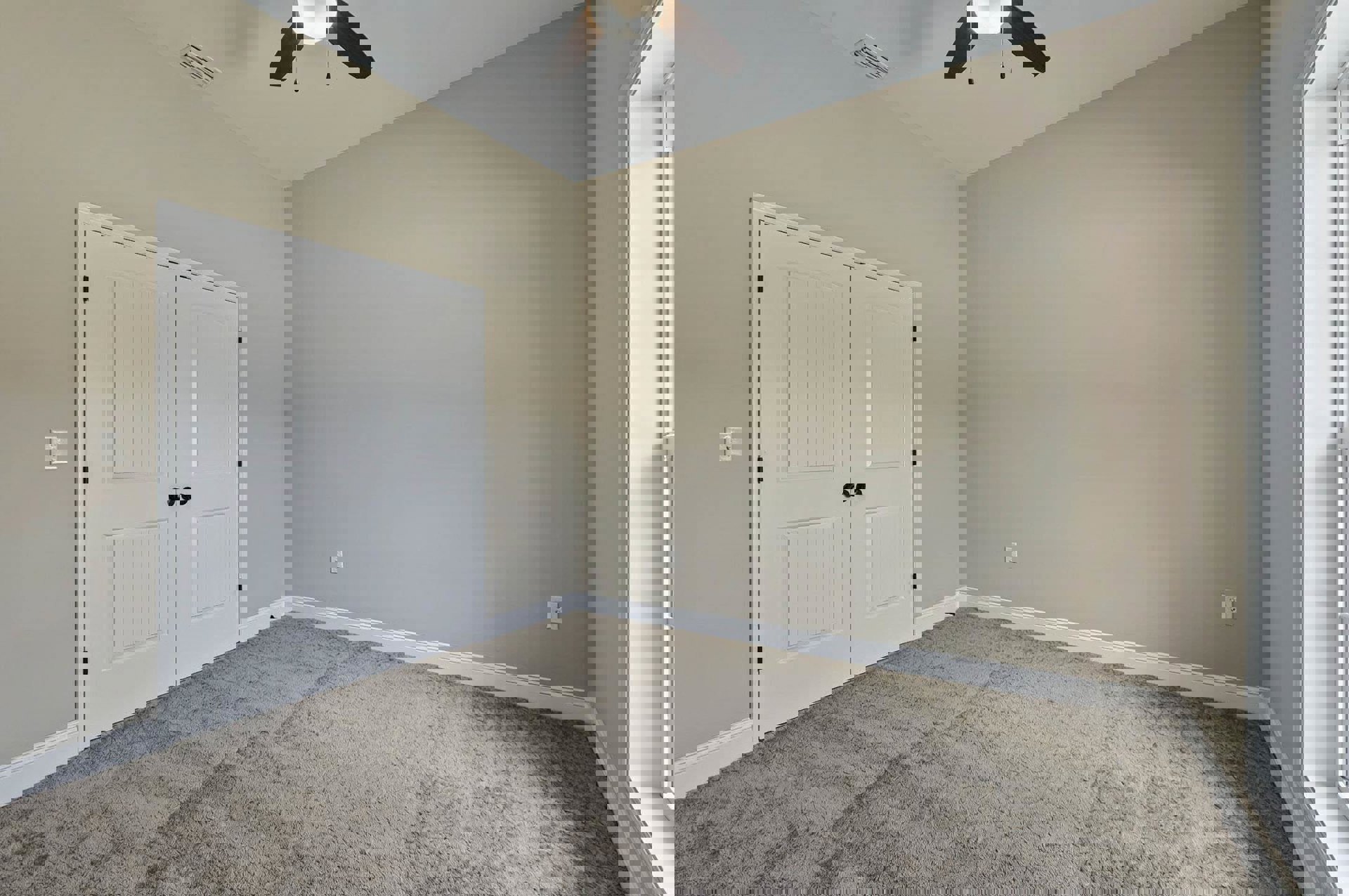 Carpeted room with white double doors featuring black knobs, white framed single door, ceiling fan, and overhead light fixture.