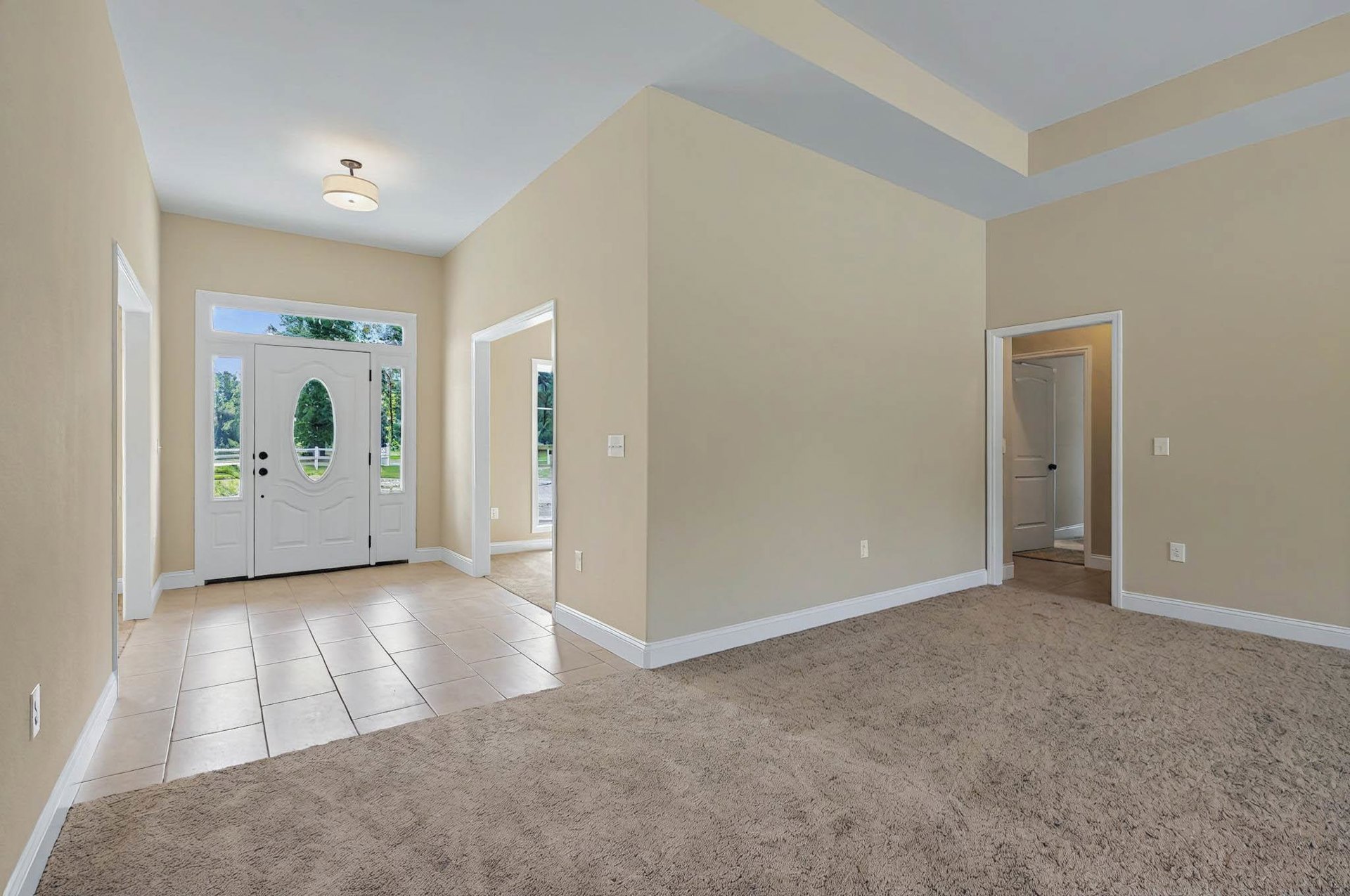 Beige carpeted floor and beige walls, white door with window and black handle, white ceiling, light fixture with white shade in corner of room