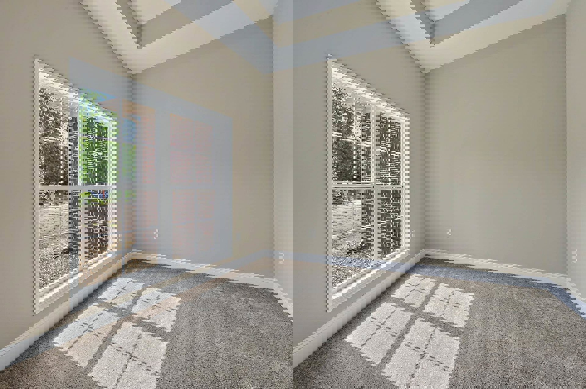 Carpeted room featuring a large window set in a brick wall, white ceiling, and patterned grey and white square carpet with views of a grassy yard outside.