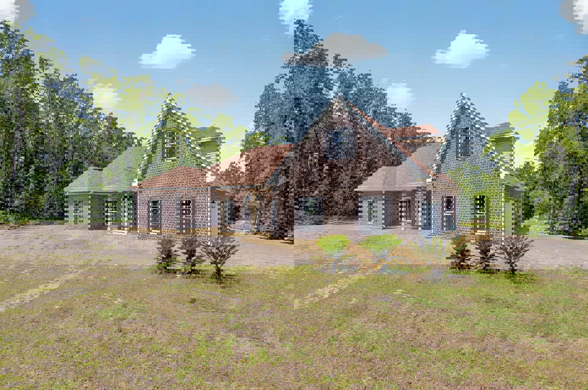 Red brick house with white roof, shuttered windows, palm trees and grass lawn, paved driveway, partly cloudy sky