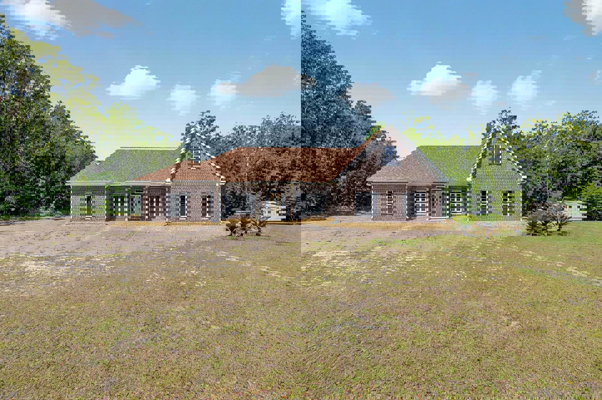 Brick farmhouse with white roof, expansive grassy yard, white-framed windows, and mature trees under a partly cloudy sky