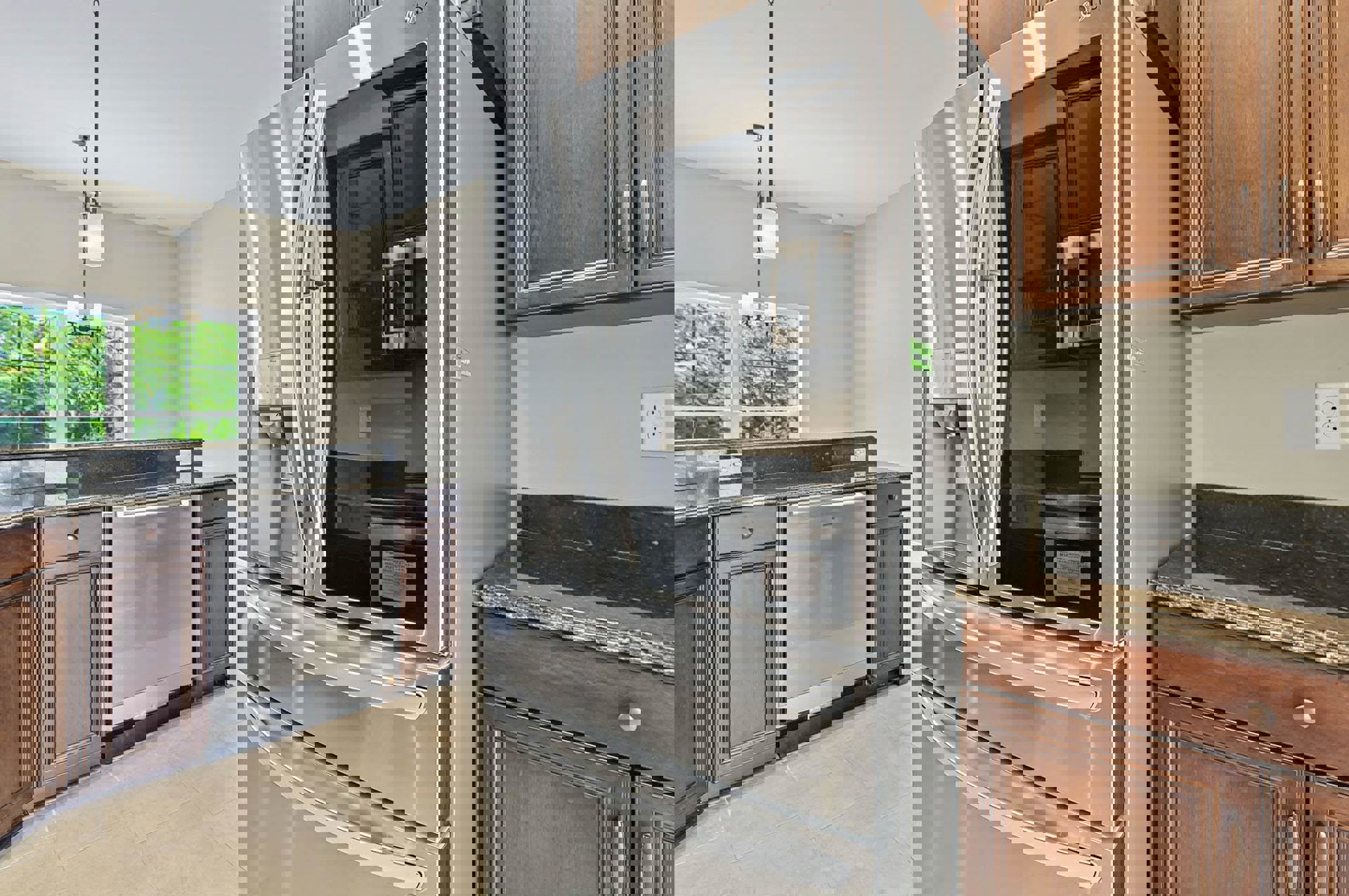 Stainless steel refrigerator with glass door beside white cabinetry, built-in dishwasher, marble countertops, electrical outlet, and window overlooking trees