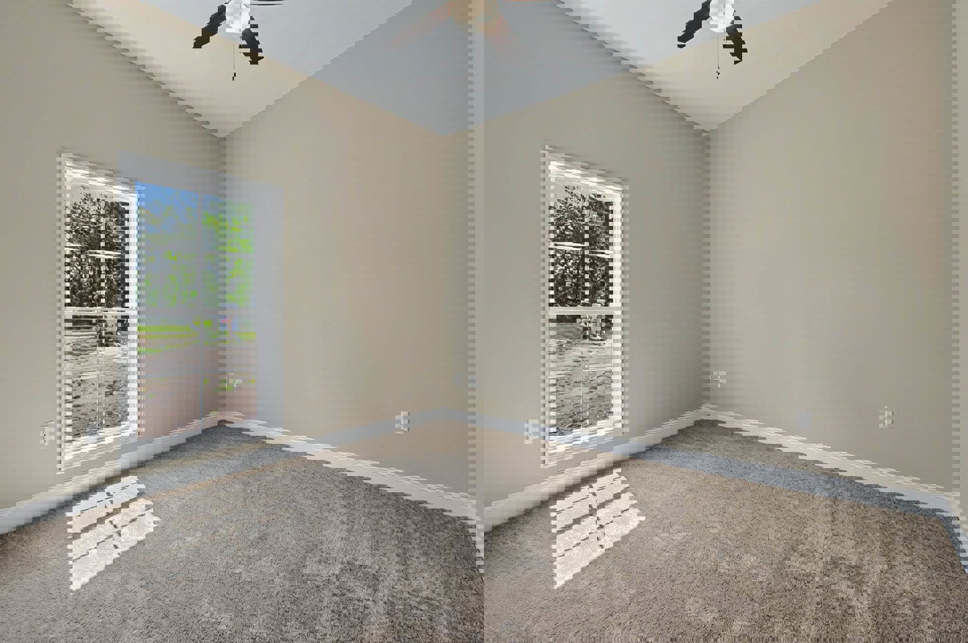 Bedroom with white carpet, large window overlooking playground, ceiling fan with light fixture, white walls, and simple molding.