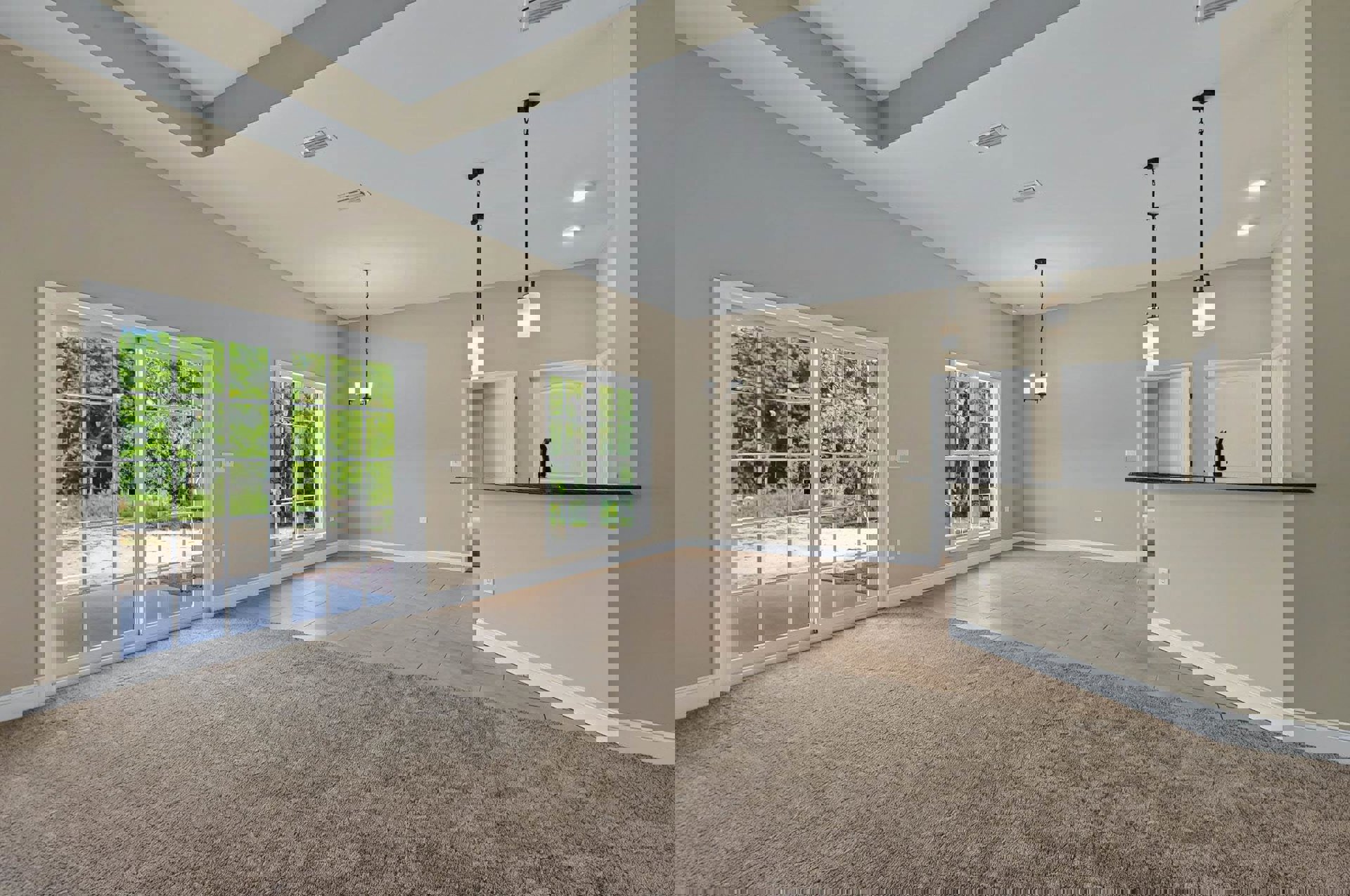 Open-concept living room with brown carpet, adjacent kitchen featuring white cabinetry and faucet, bar area, multi-pane window, sliding glass door overlooking trees, black floor