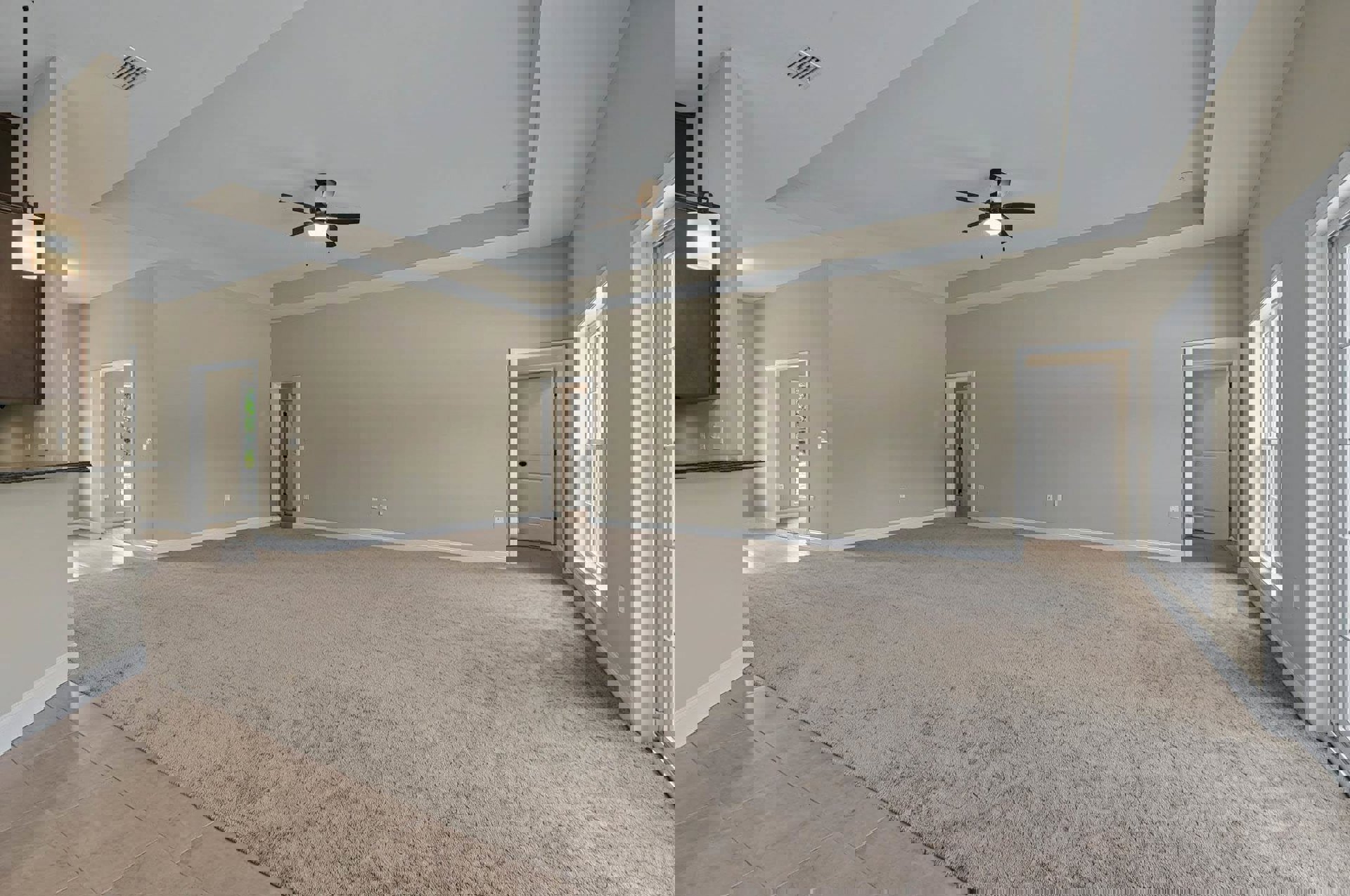 Spacious carpeted room featuring a ceiling fan with light, white door with black handle, wall vent, and white baseboard molding