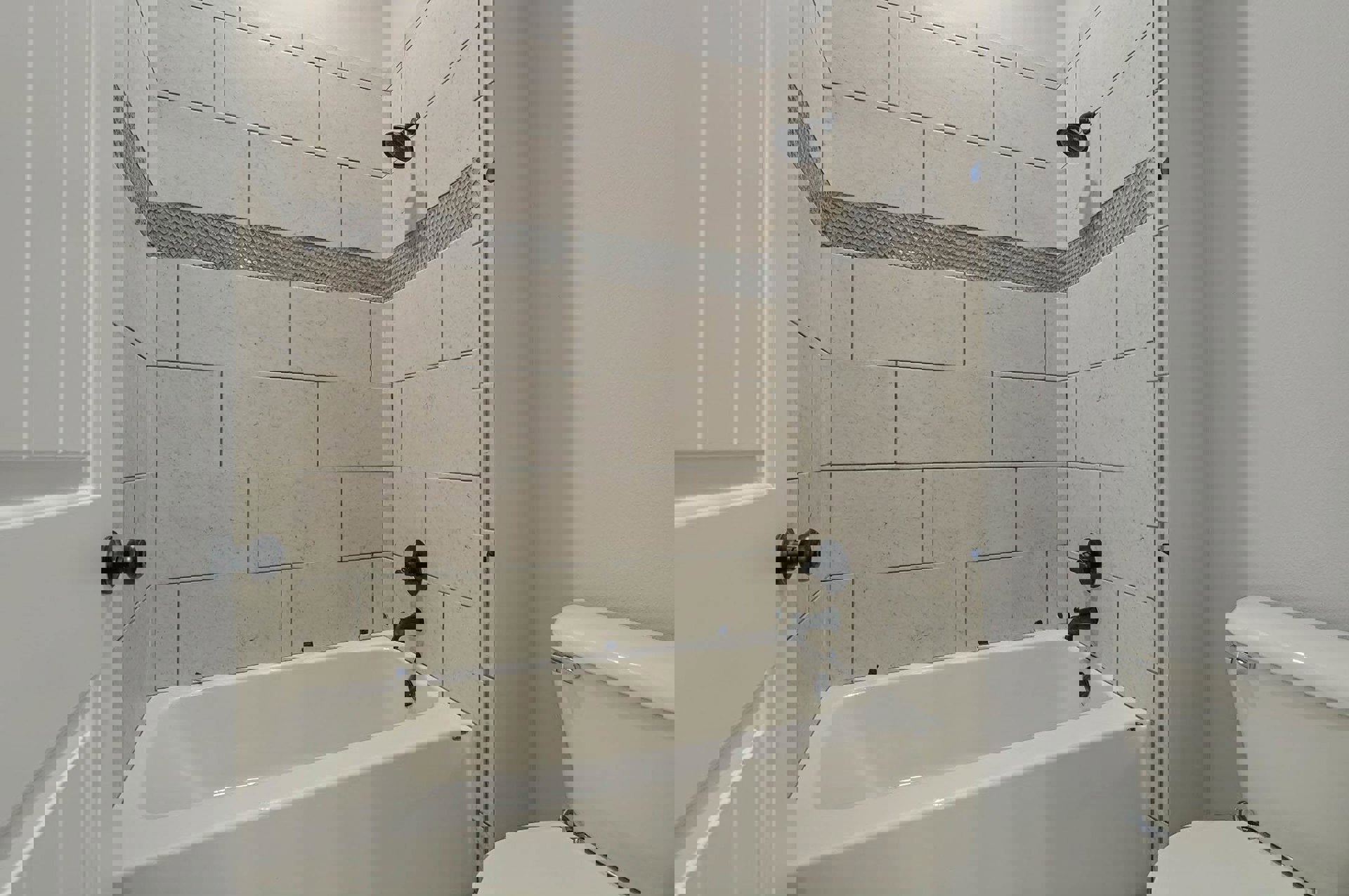 White-tiled bathroom with freestanding tub, modern silver-handled toilet, black shower head, black door knob, and a person’s foot in a black sock visible near the tub