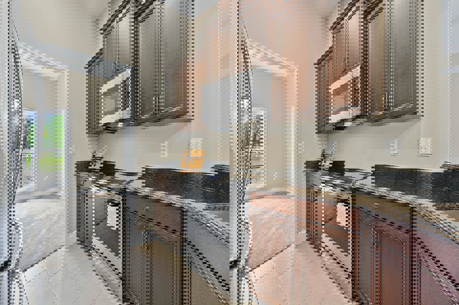 Dark wood kitchen cabinets, stainless steel microwave with open door, paper stuck in oven door, white double light switch on wall, wooden box with black ribbon on countertop.