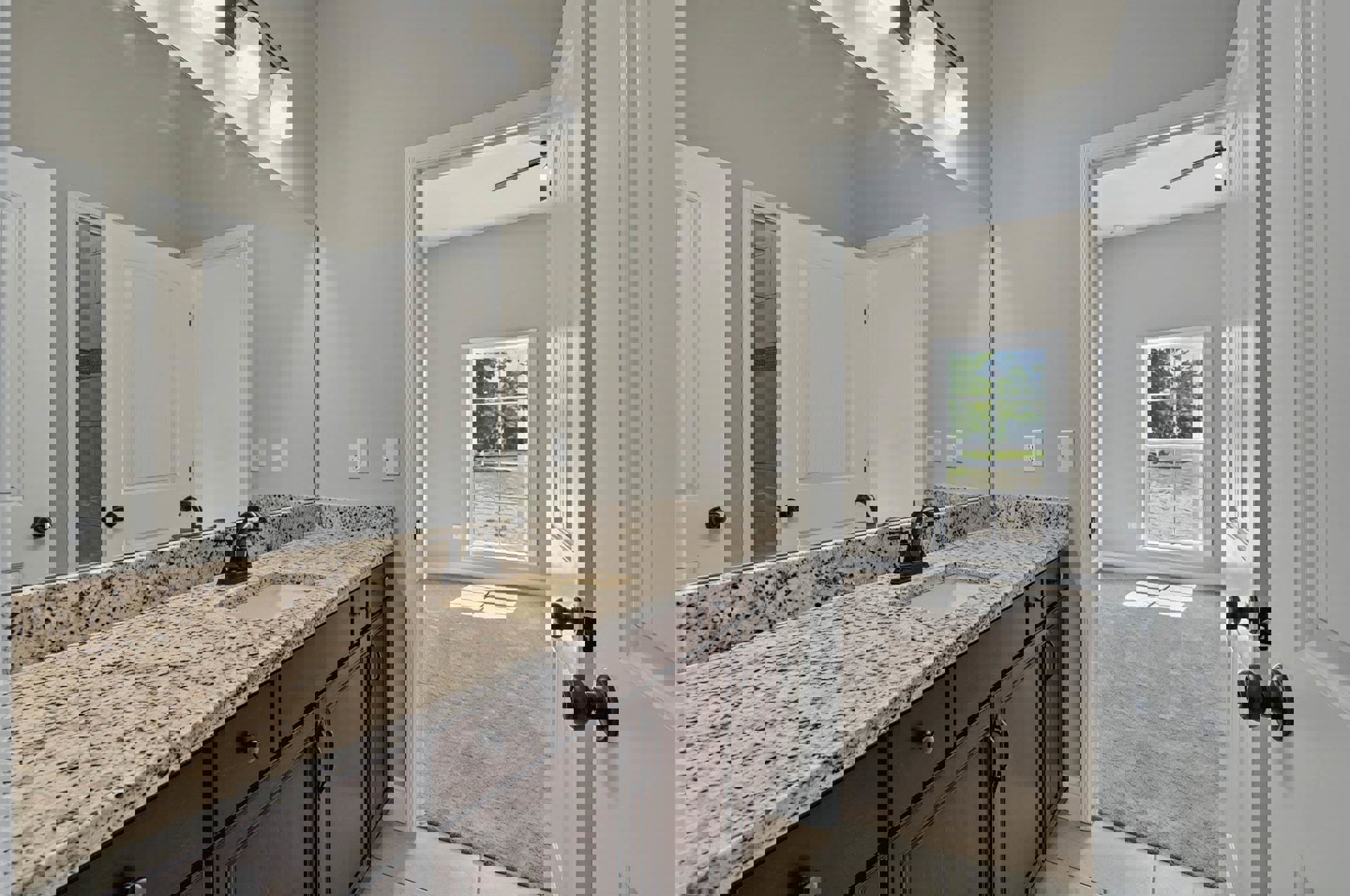 Bathroom featuring a marble countertop with undermount sink, framed mirror above, white cabinetry, tile backsplash, and a door leading to adjacent space; window offers view of